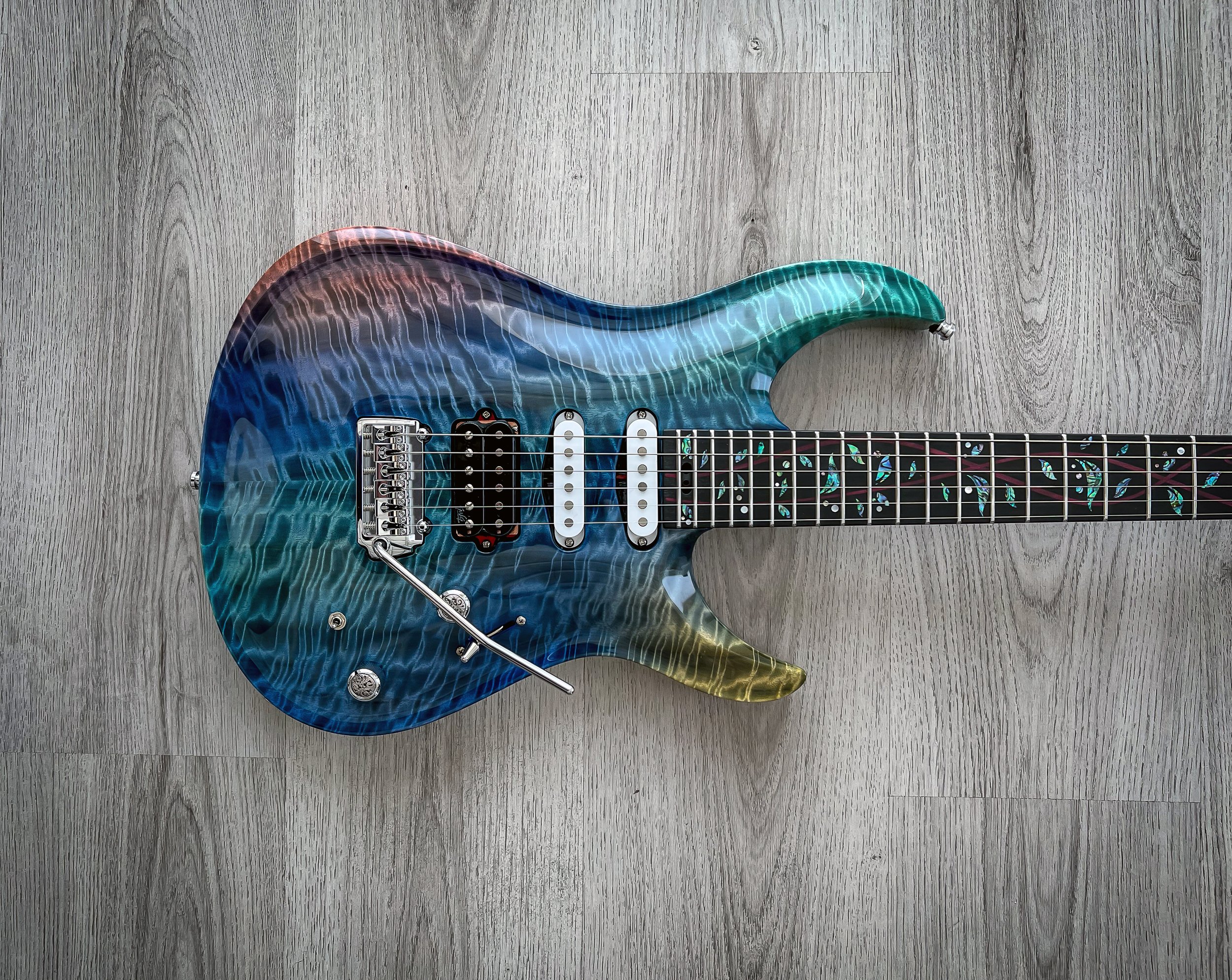GNG Giulio Negrini electric guitar with a colorful, wavy pattern finish, featuring multiple pickups, a tremolo bar, and a decorative fretboard inlay, lying on a wooden surface.