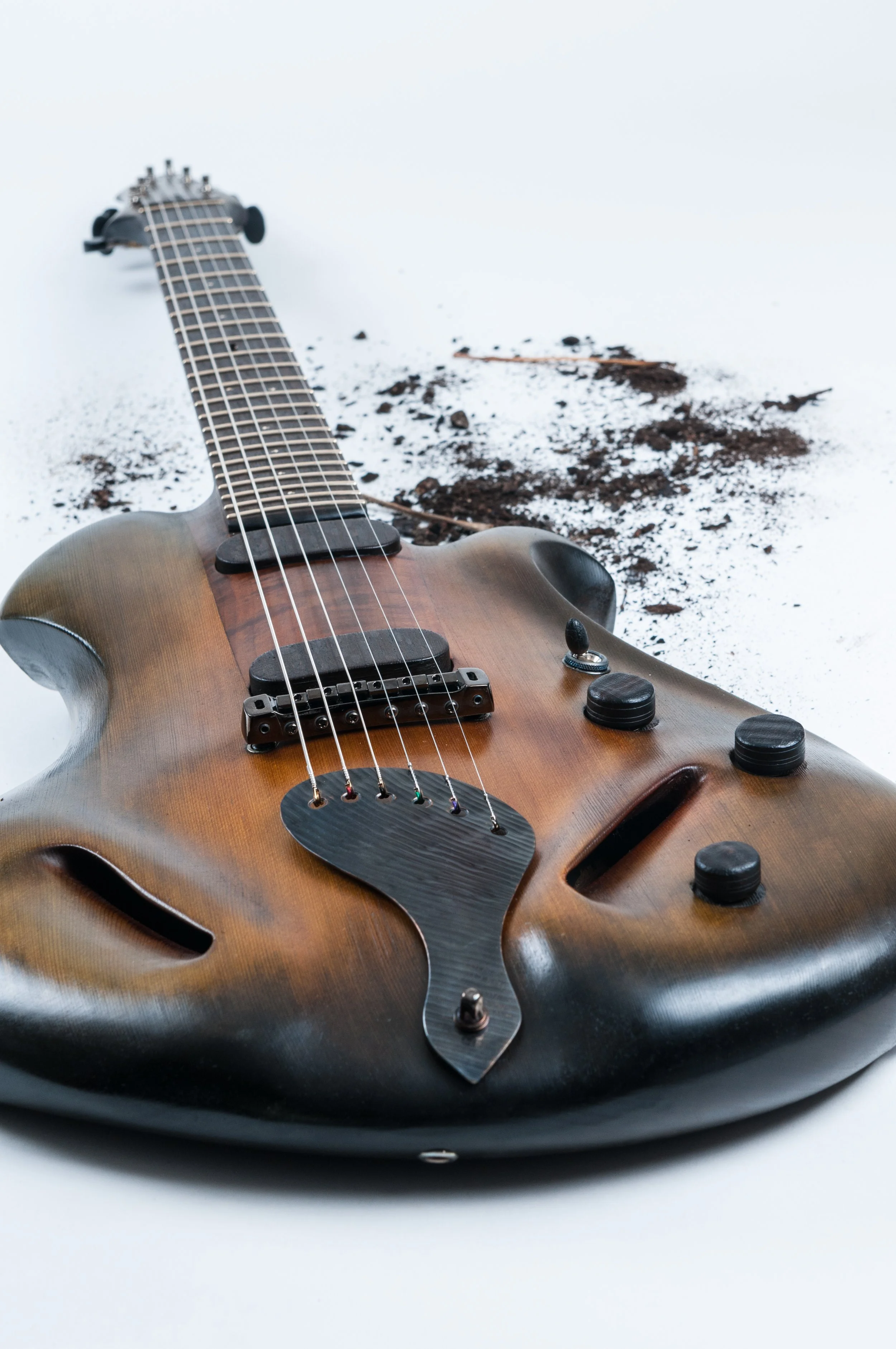 An electric Ergon guitar lying on a white surface with soil and dirt nearby.