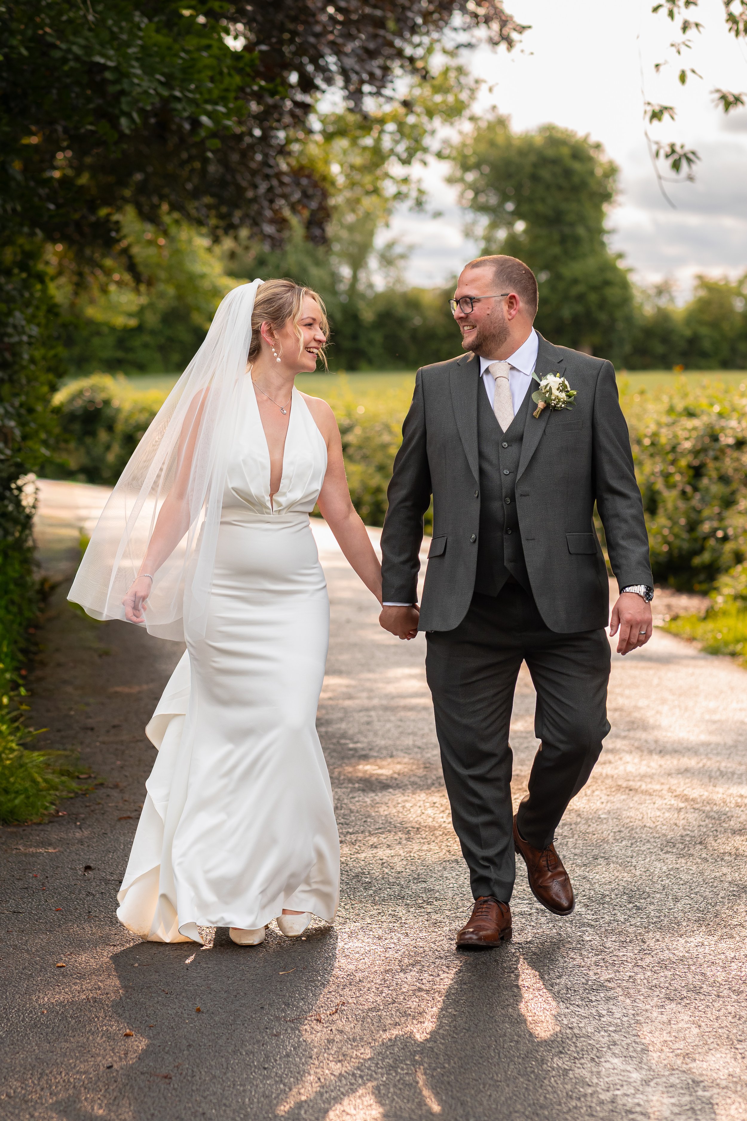 A smiling couple in formal wedding attire embracing outdoors near a pond.