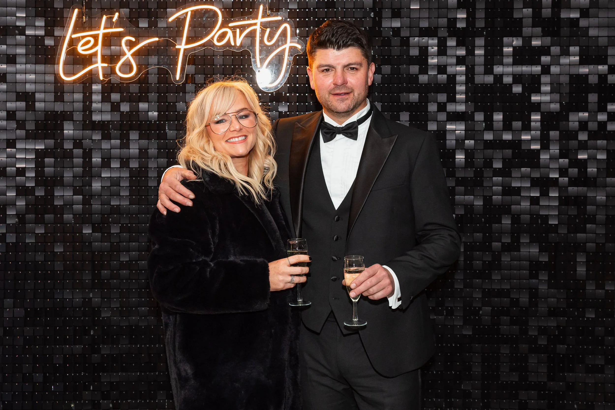 Natural party portrait of guests at a Cheshire birthday celebration in front of a ‘Let’s Party’ backdrop.