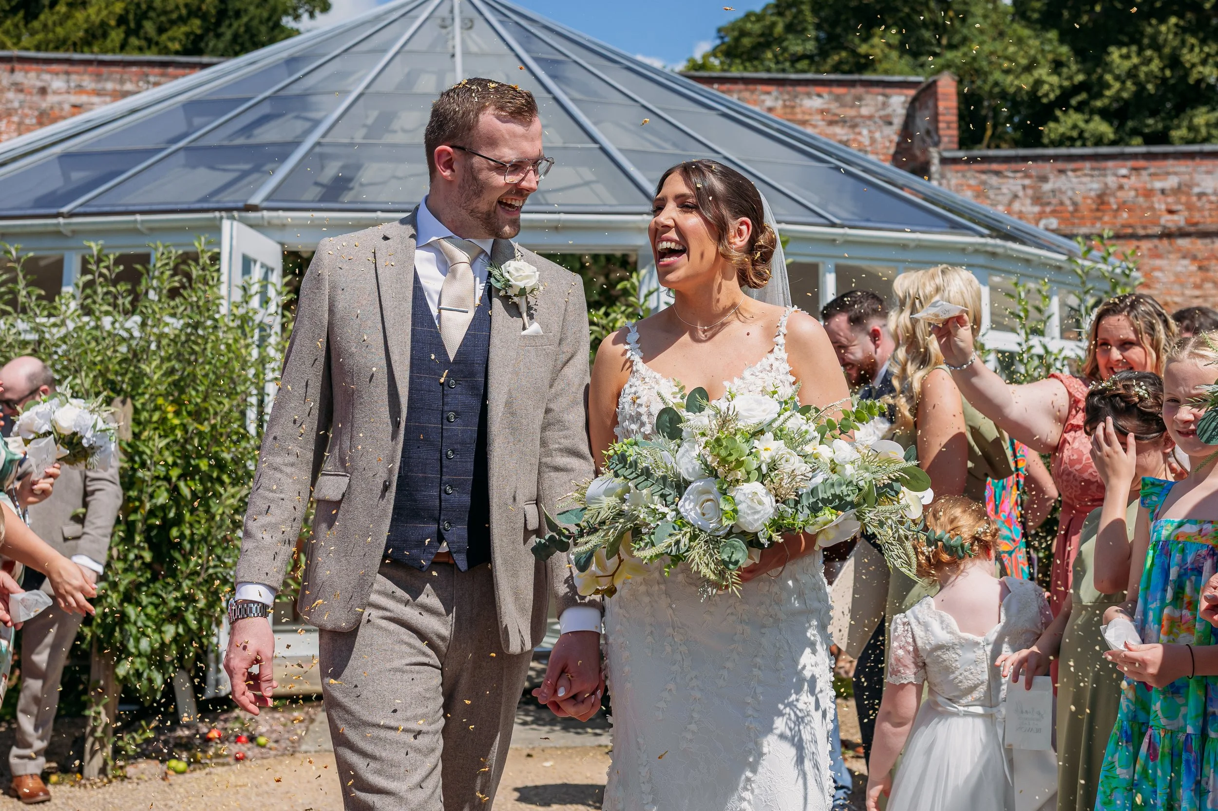 Bride and groom laughing as guests throw confetti after their wedding ceremony at a Cheshire wedding venue Combermere Abbey