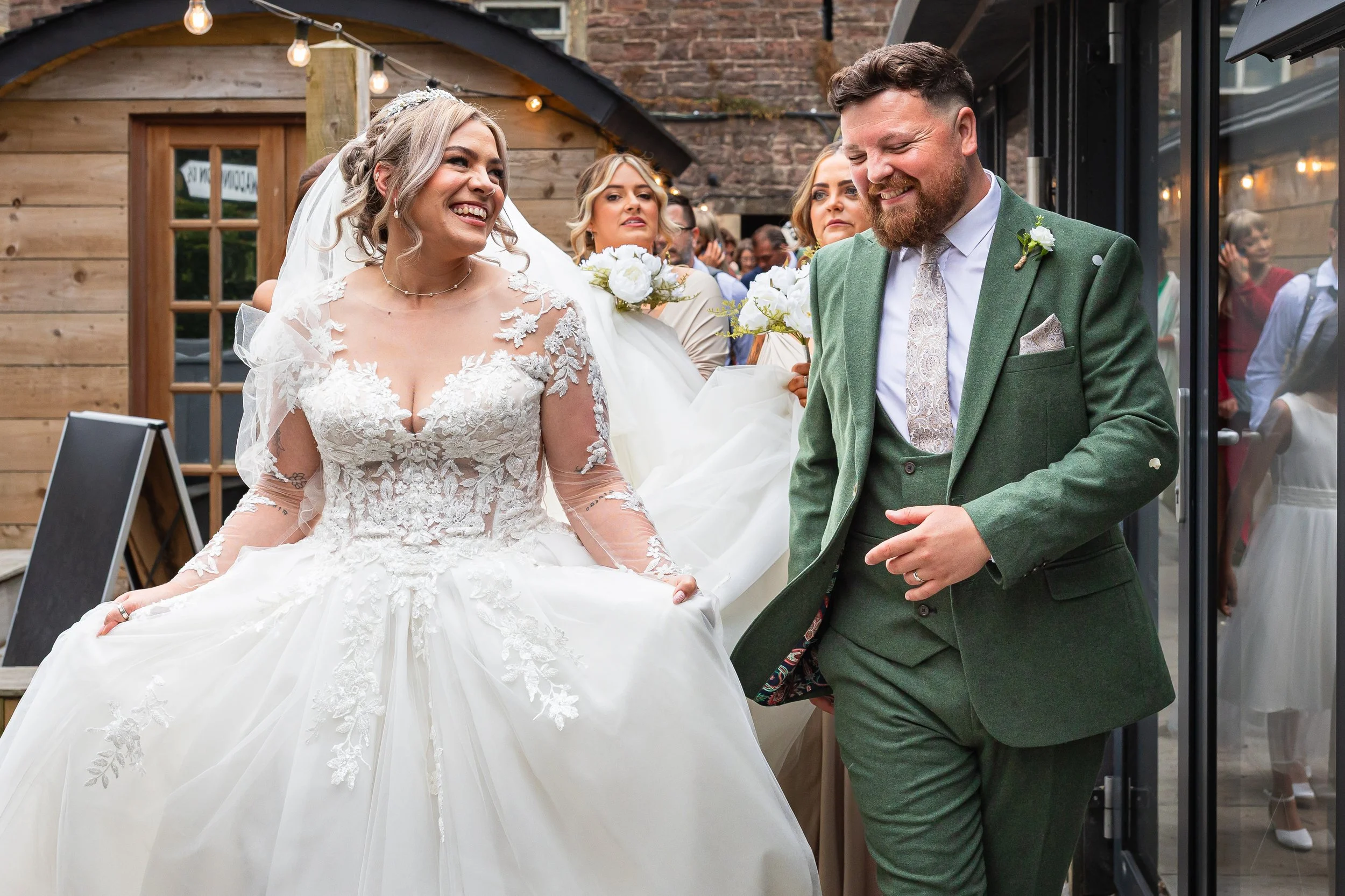 Bride and groom walking into their drinks reception after the ceremony at a Cheshire wedding, smiling and celebrating with friends behind them.