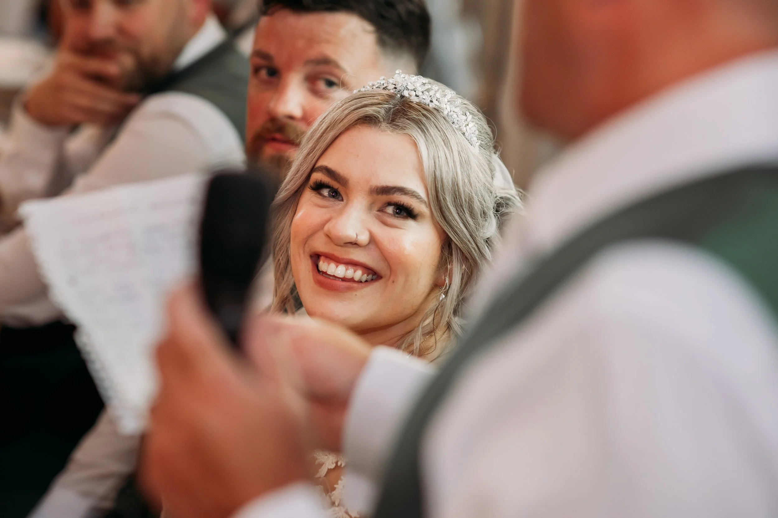 Bride smiling and reacting to a speech during the wedding breakfast at Bashall Barn in Lancashire