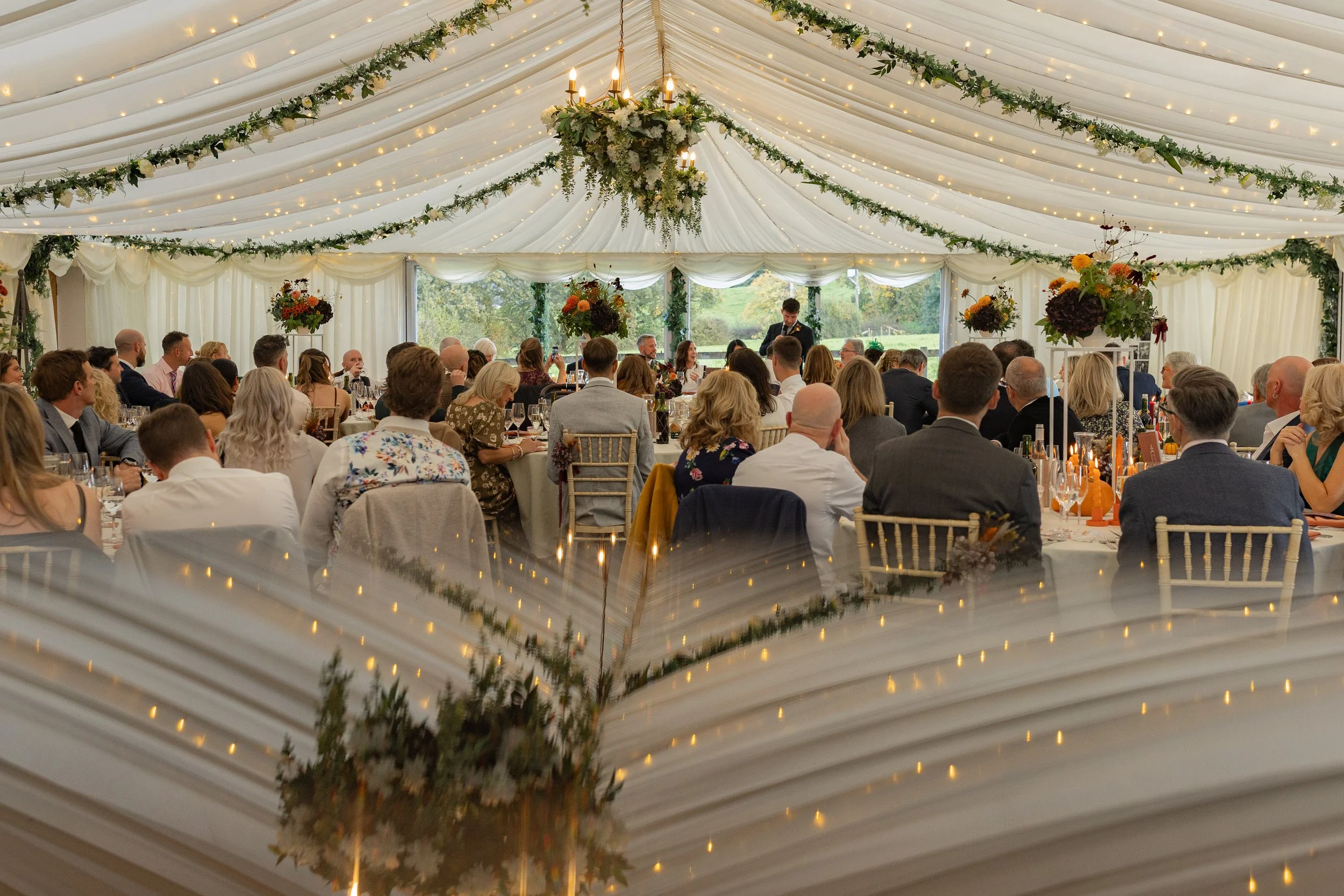 Wide view of guests listening to wedding speeches inside the marquee at Hilltop Country House in Cheshire