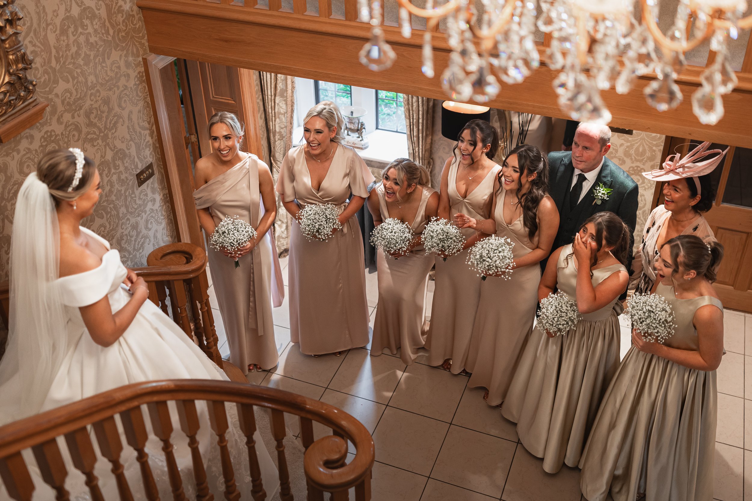 Bridesmaids reacting to the bride on the staircase during morning preparations at Merrydale Manor in Cheshire