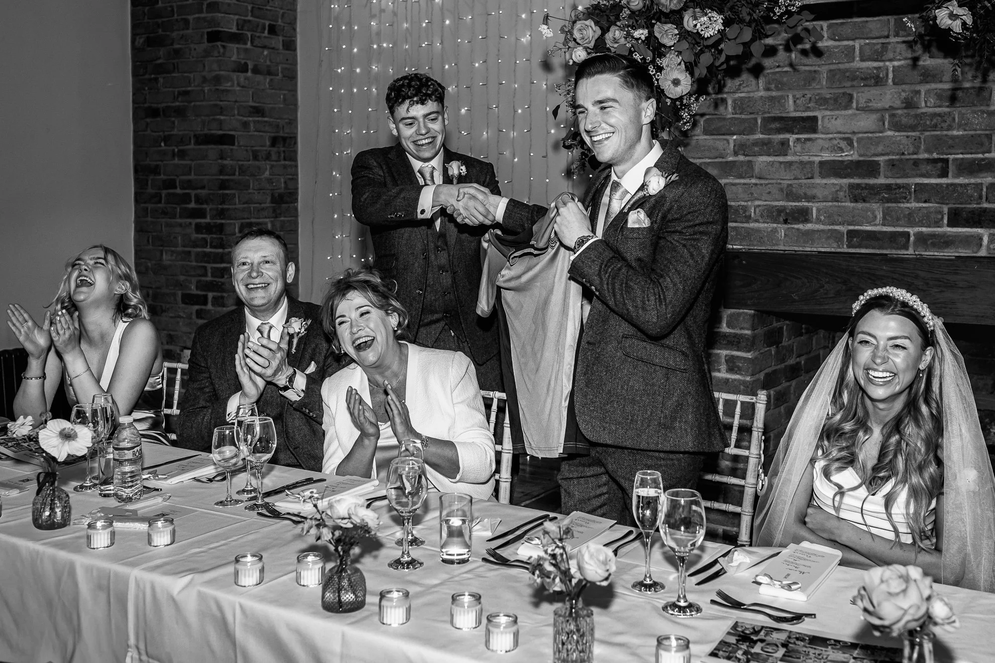Wedding speeches in Cheshire as the top table bursts into laughter, captured in a joyful and candid documentary moment.
