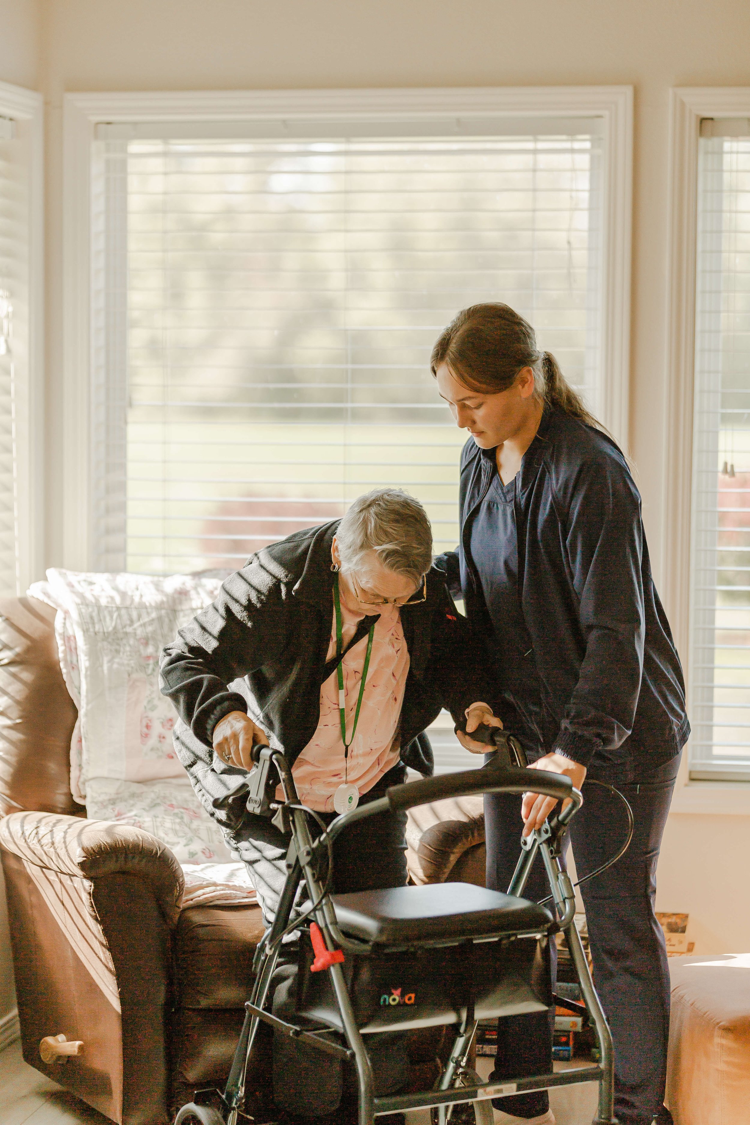 An Elderly resident of Belamour Care using a walker assisted by a Belamour caregiver in a living room of one of our Assisted Senior Living Homes in Washington State.
