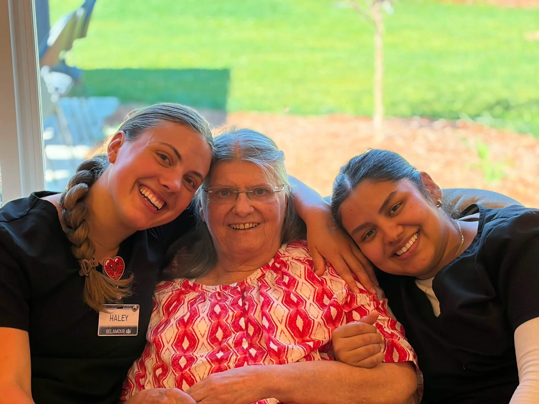 Group of elderly people working on a puzzle at a table, with one person in a wheelchair, in a communal space of a Belamour Care Assisted Senior Living facility.