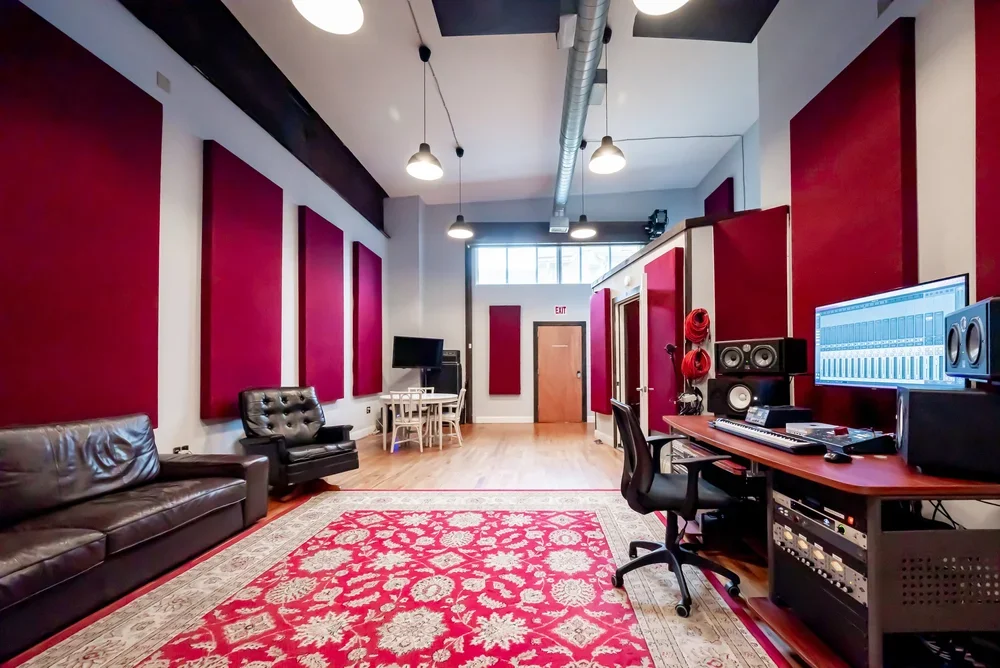 Recording studio with red and white acoustic panels, leather couches, a rug, and audio production equipment.