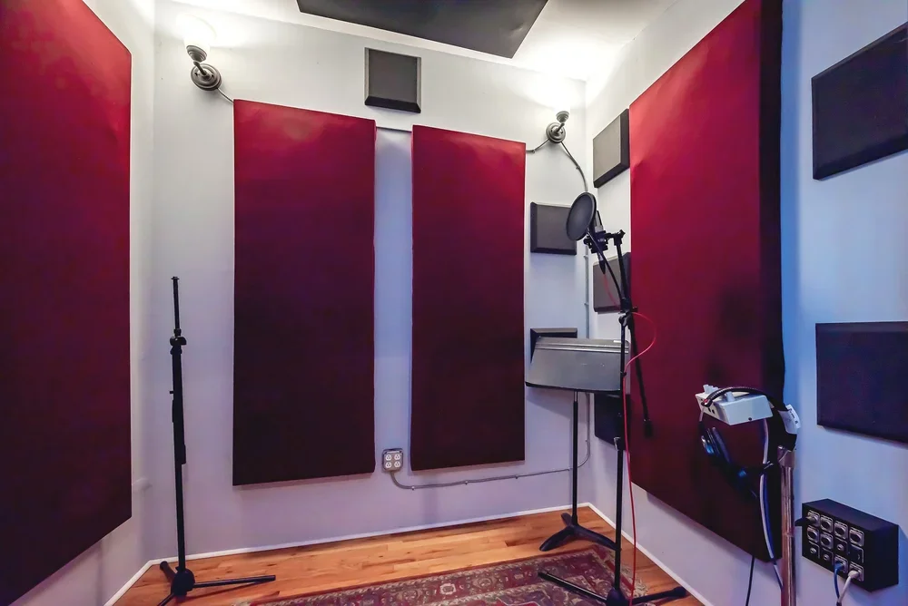 Recording studio with red and black acoustic panels, microphone on stand, headphones, and audio equipment.