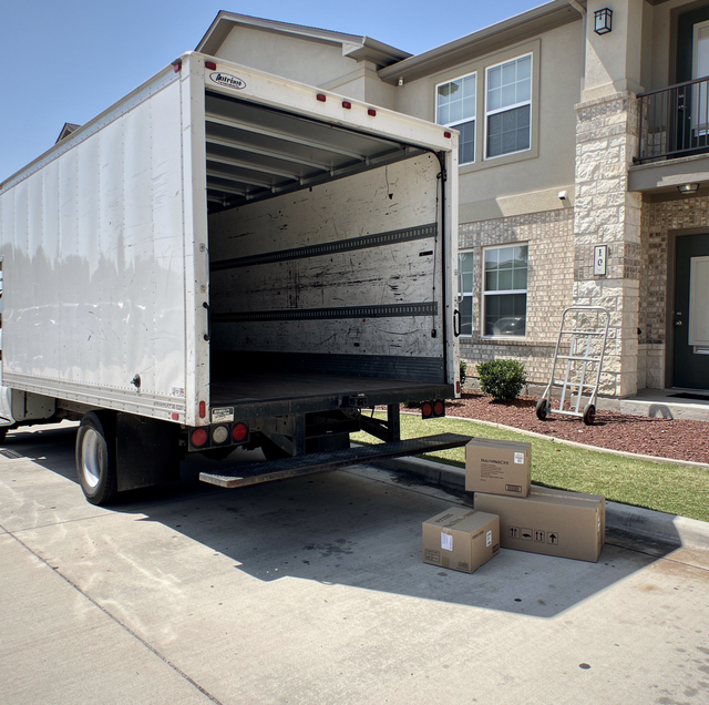 Moving truck with open rear door backed up to house driveway with cardboard boxes on ground