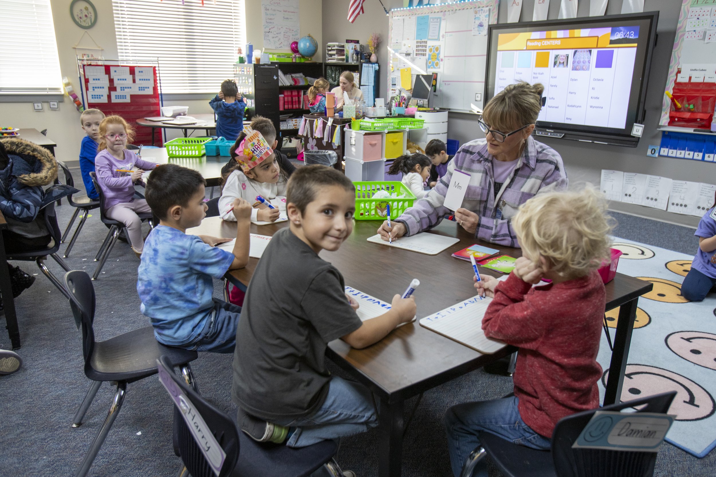  A group of Union Colony students are sitting at a table in an Elementary School classroom with their teacher. 