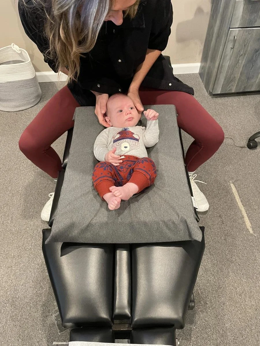 Infant in a striped onesie lying on the pediatric adjustment table while the chiropractor secures the safety strap — pediatric chiropractic care in Solana Beach