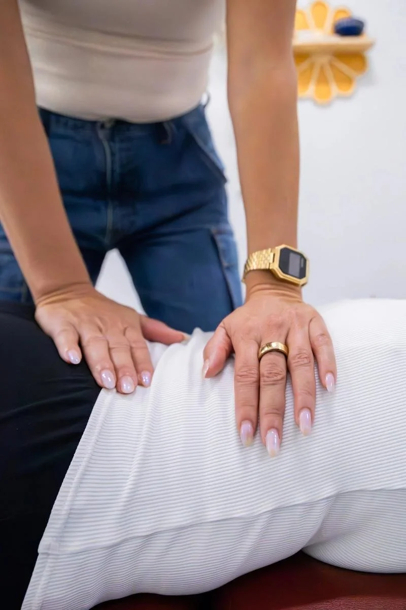 Close-up of hands performing a prone low back adjustment on a postpartum patient in a white skirt and jeans — postpartum chiropractic care in Solana Beach
