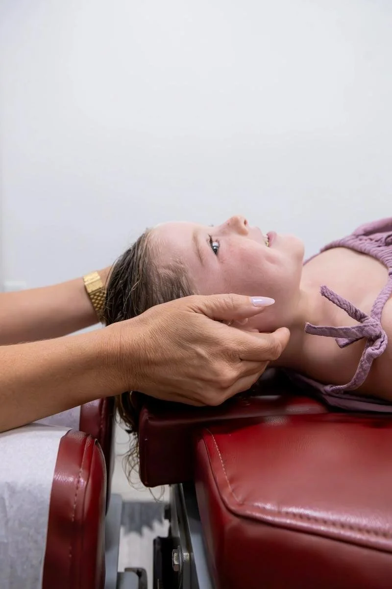 Close-up of hands cradling the patient's head during a gentle upper cervical adjustment on the red table — chiropractic care for Cardiff-by-the-Sea patients