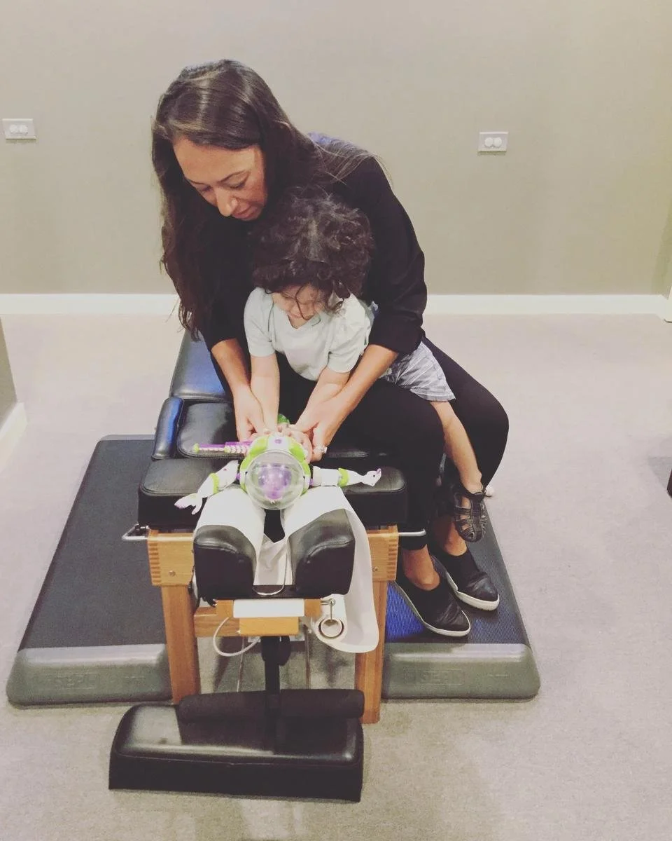 Dr. Lisel guiding a small child seated on the Buzz Lightyear pelvic adjustment trainer on the drop table — pediatric chiropractic care in Solana Beach