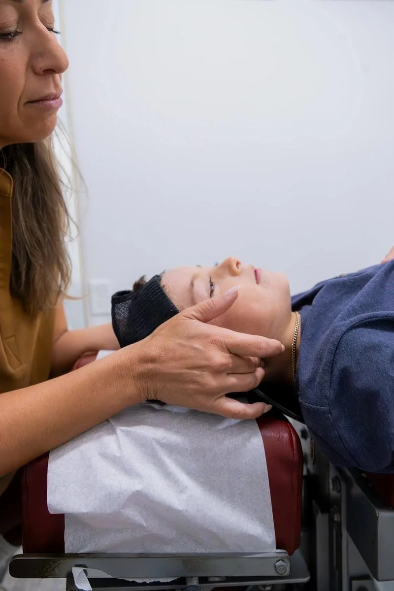 Close-up of hands cradling a supine patient's head for a gentle cervical adjustment on the red table — chiropractic care for Rancho Santa Fe patients