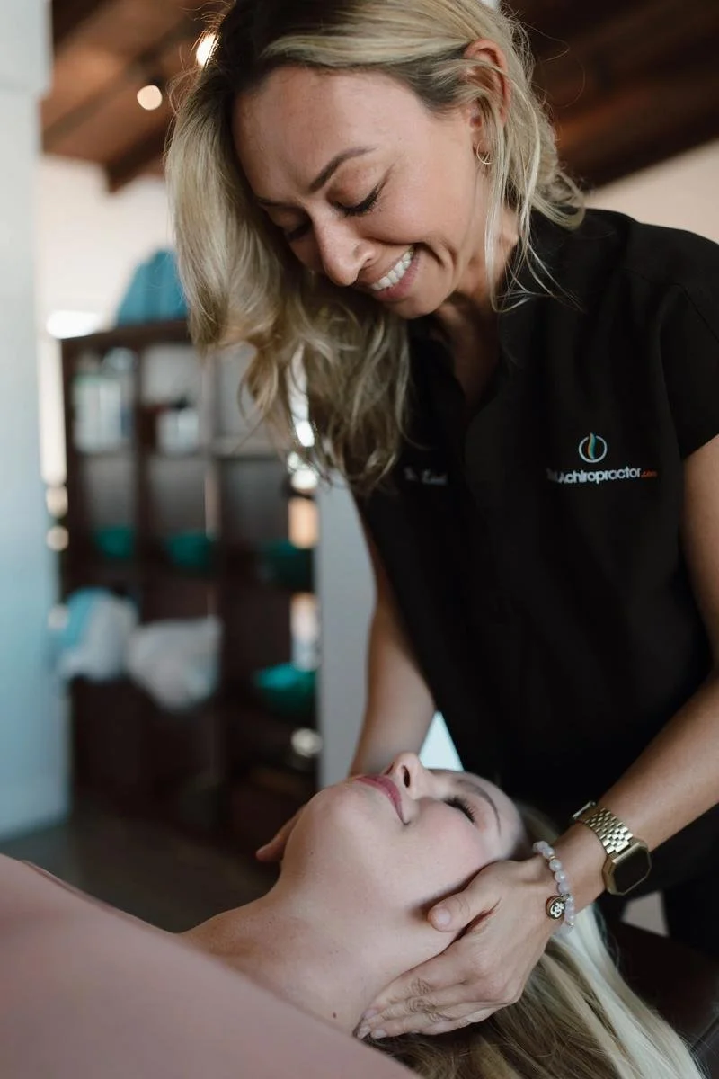 Female chiropractor in a black top performing a gentle cervical adjustment on a patient lying supine — chiropractic care for Cardiff-by-the-Sea patients
