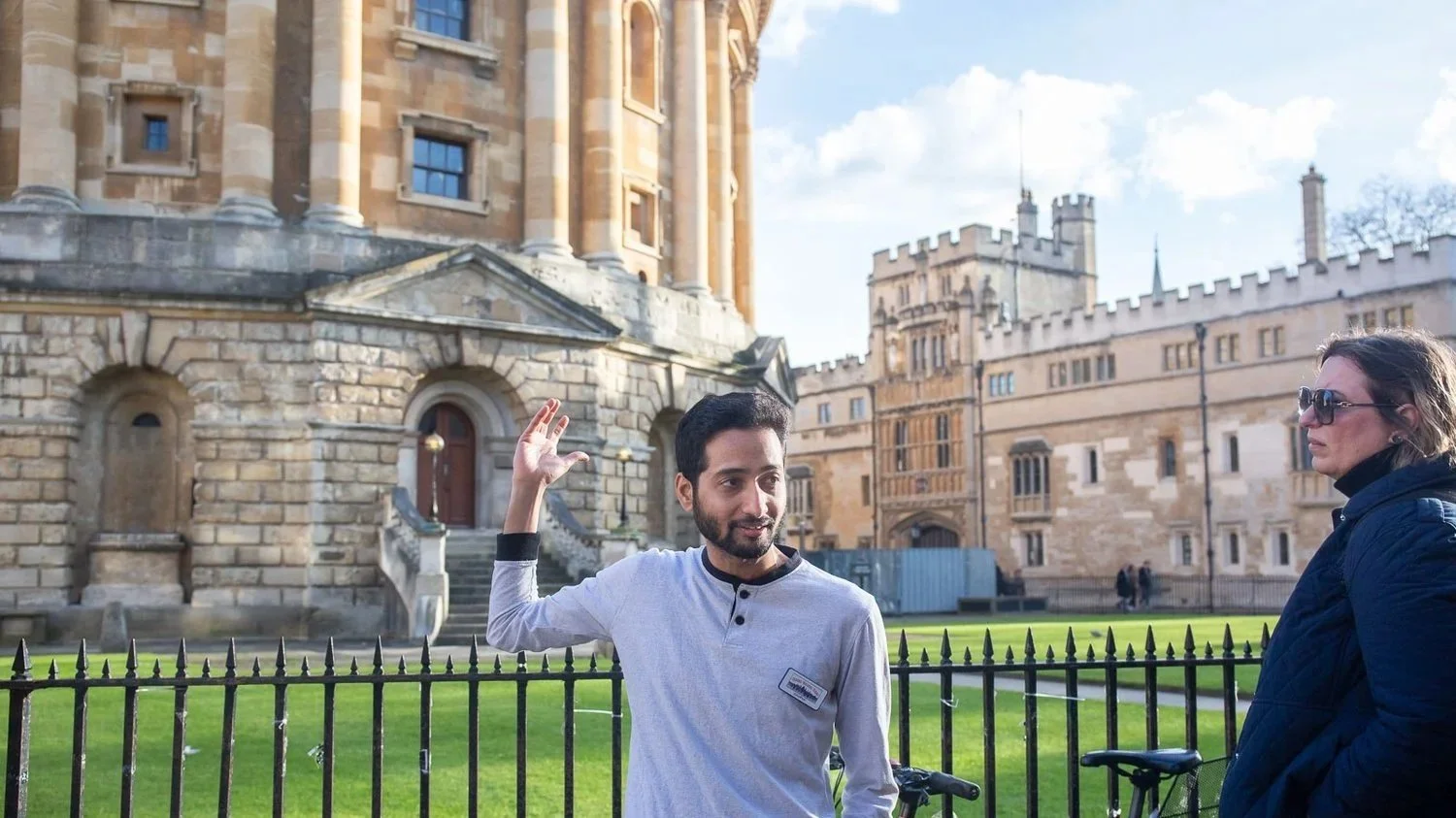 An Oxford student guide gives a private tour to a small family on the lunch and tour with an Oxford student experience. The Oxford student gestures towards Harry Potter film sites and beautiful colleges you visit on the tour of Oxford University.