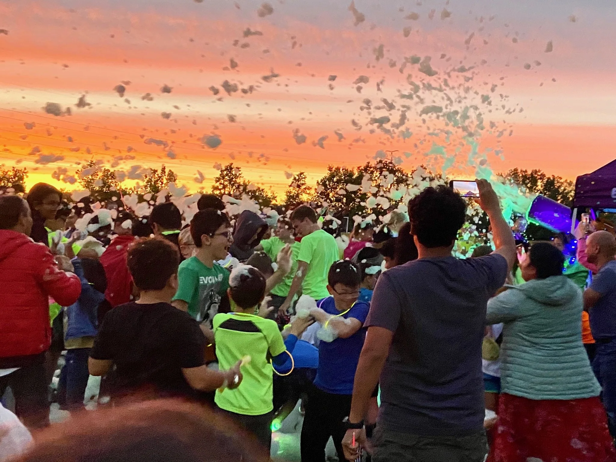 Large outdoor foam party at sunset by Varsity Foam in Chicagoland with a crowd of excited guests covered in foam