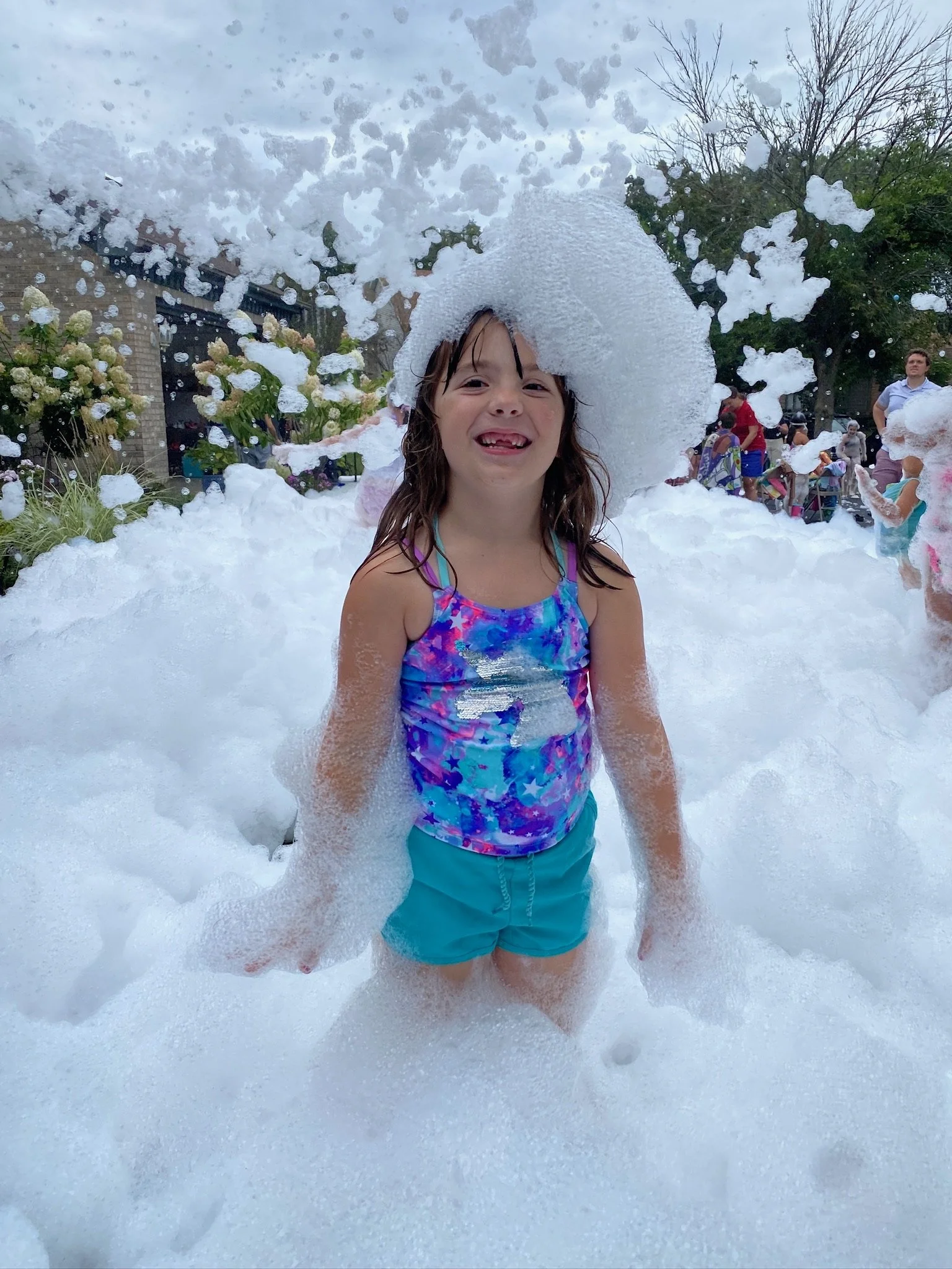 Young girl smiling at a Varsity Foam kids foam party in Chicagoland surrounded by foam at an outdoor birthday event