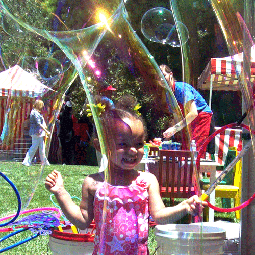 Young girl playing with giant bubble wand at a Varsity Foam bubble party in Chicagoland at an outdoor event