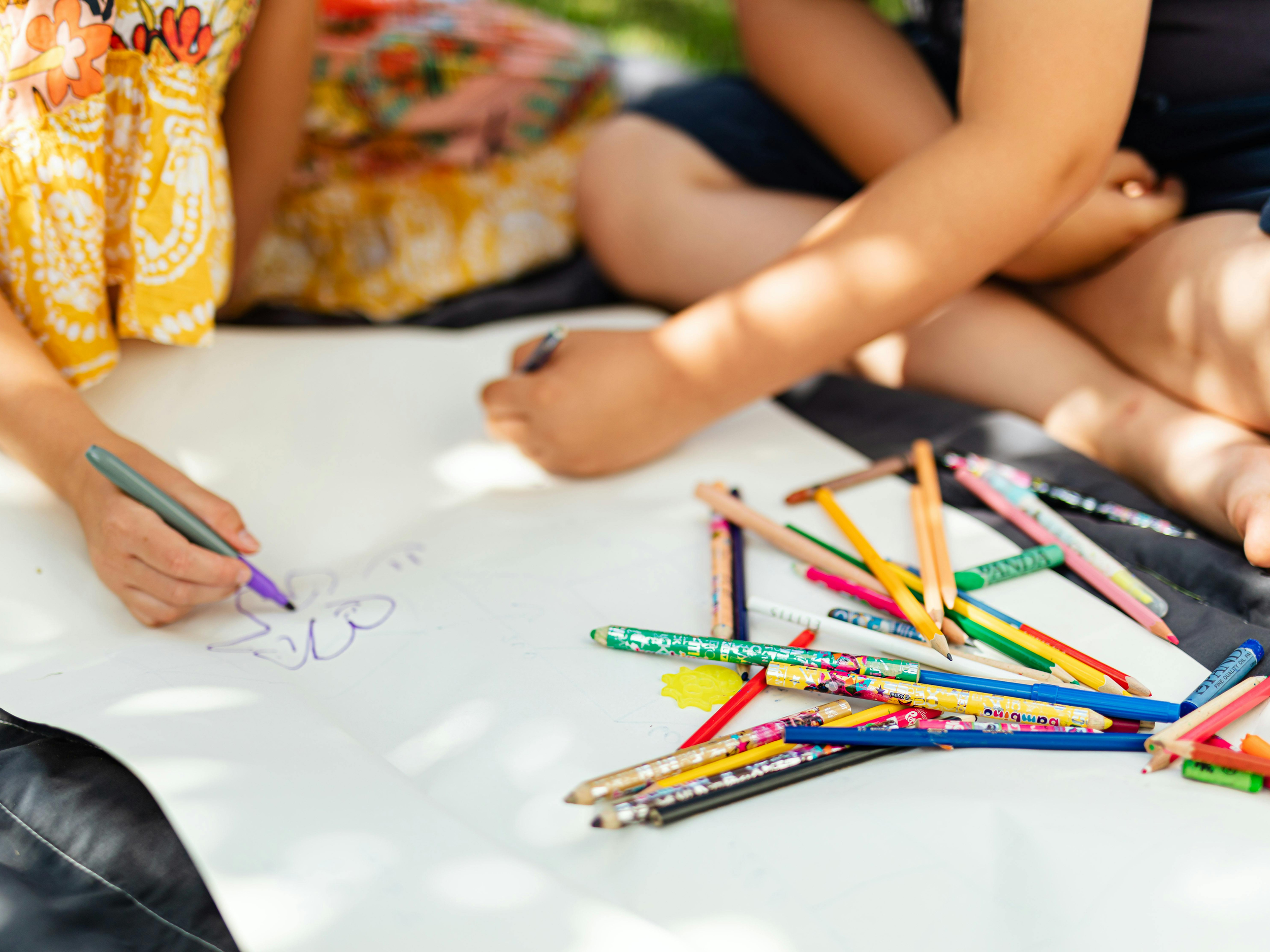 closeup of two young kids outdoors drawing and coloring on the grass