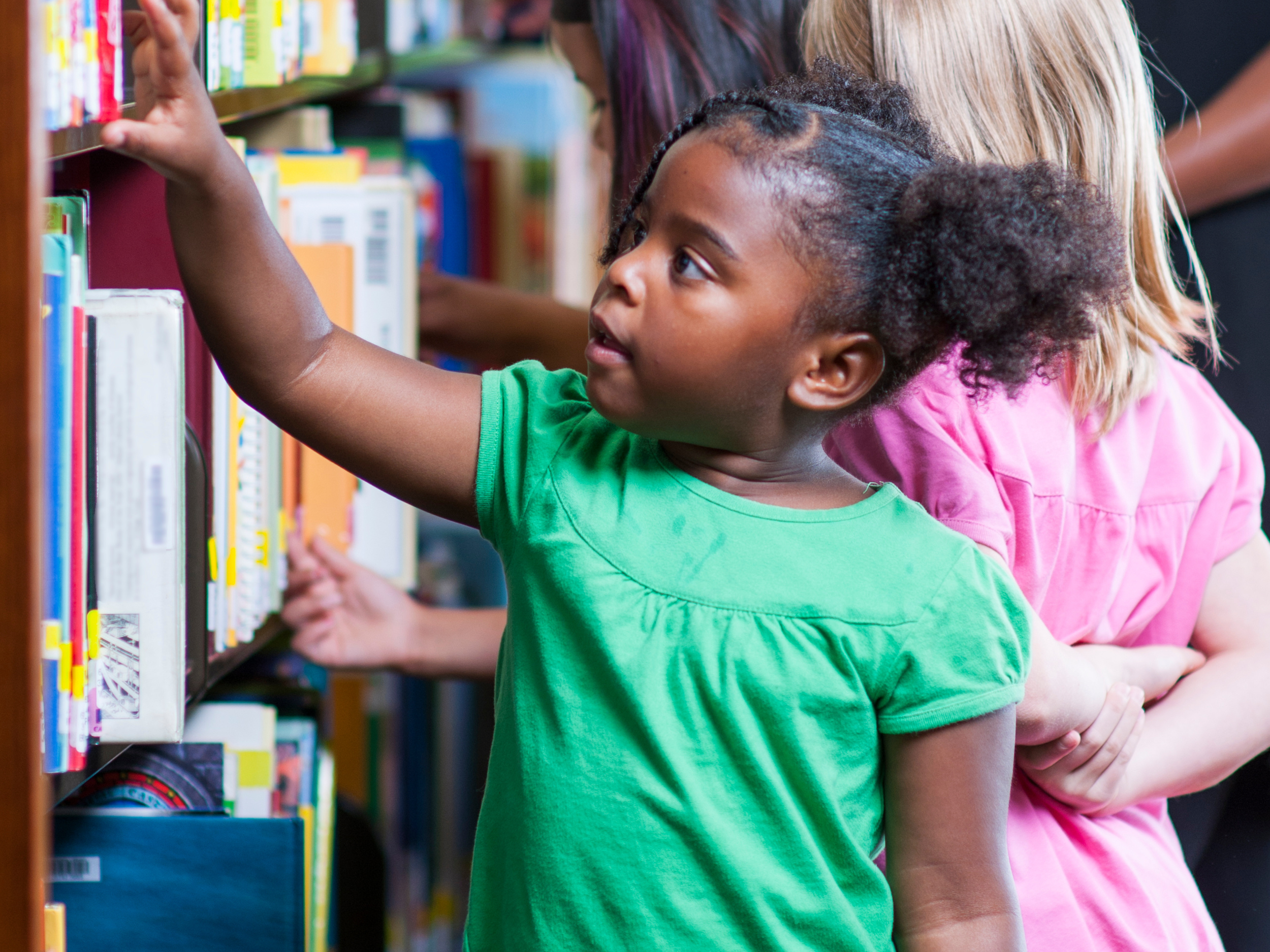 closeup of little black girl in the library looking at books on the shelf