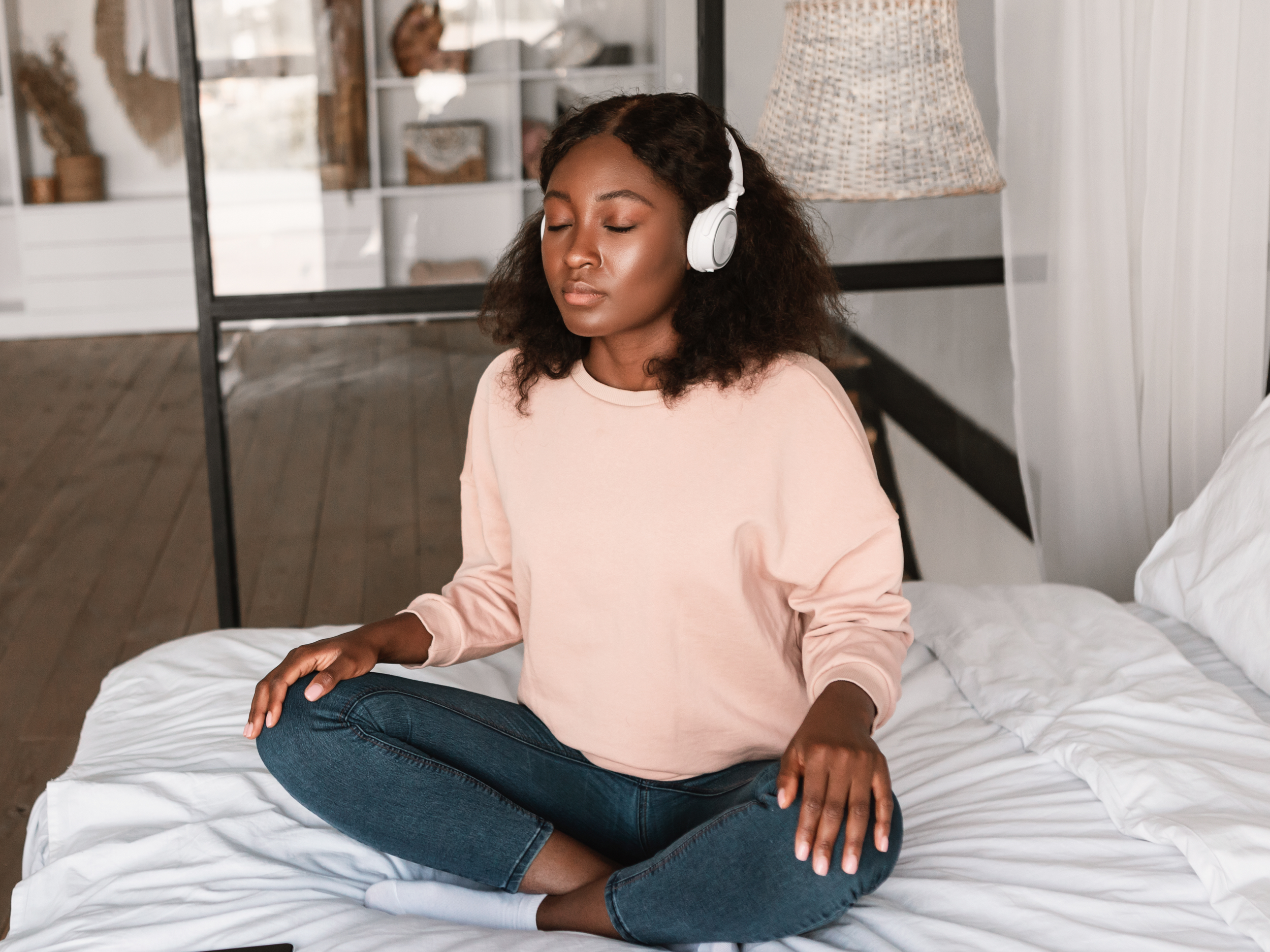 black woman sitting at home on bed with headphones on and meditating