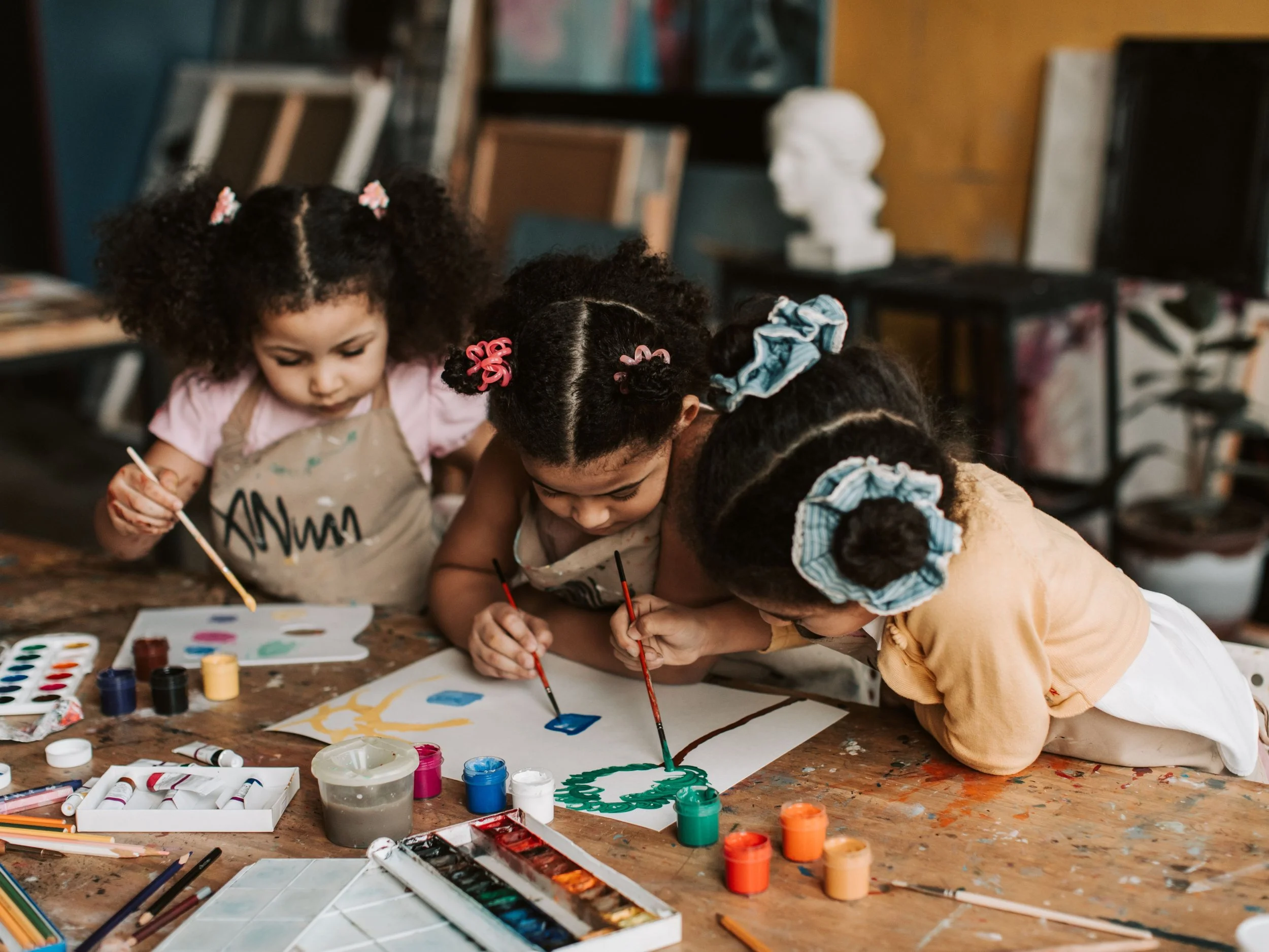 three toddler black girls at table doing arts and crafts