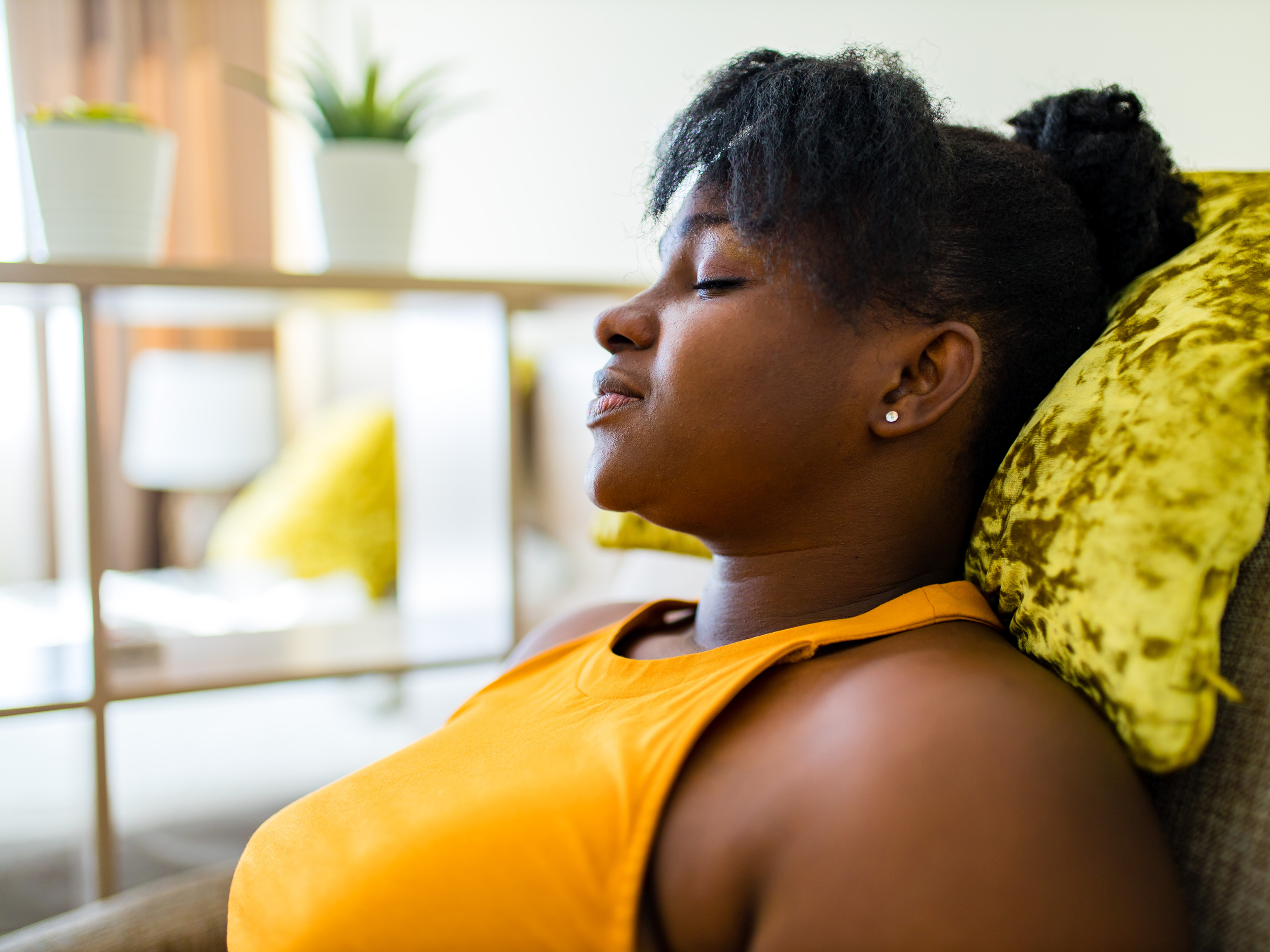 black woman, natural hair bun, at home leaning back on couch relaxing