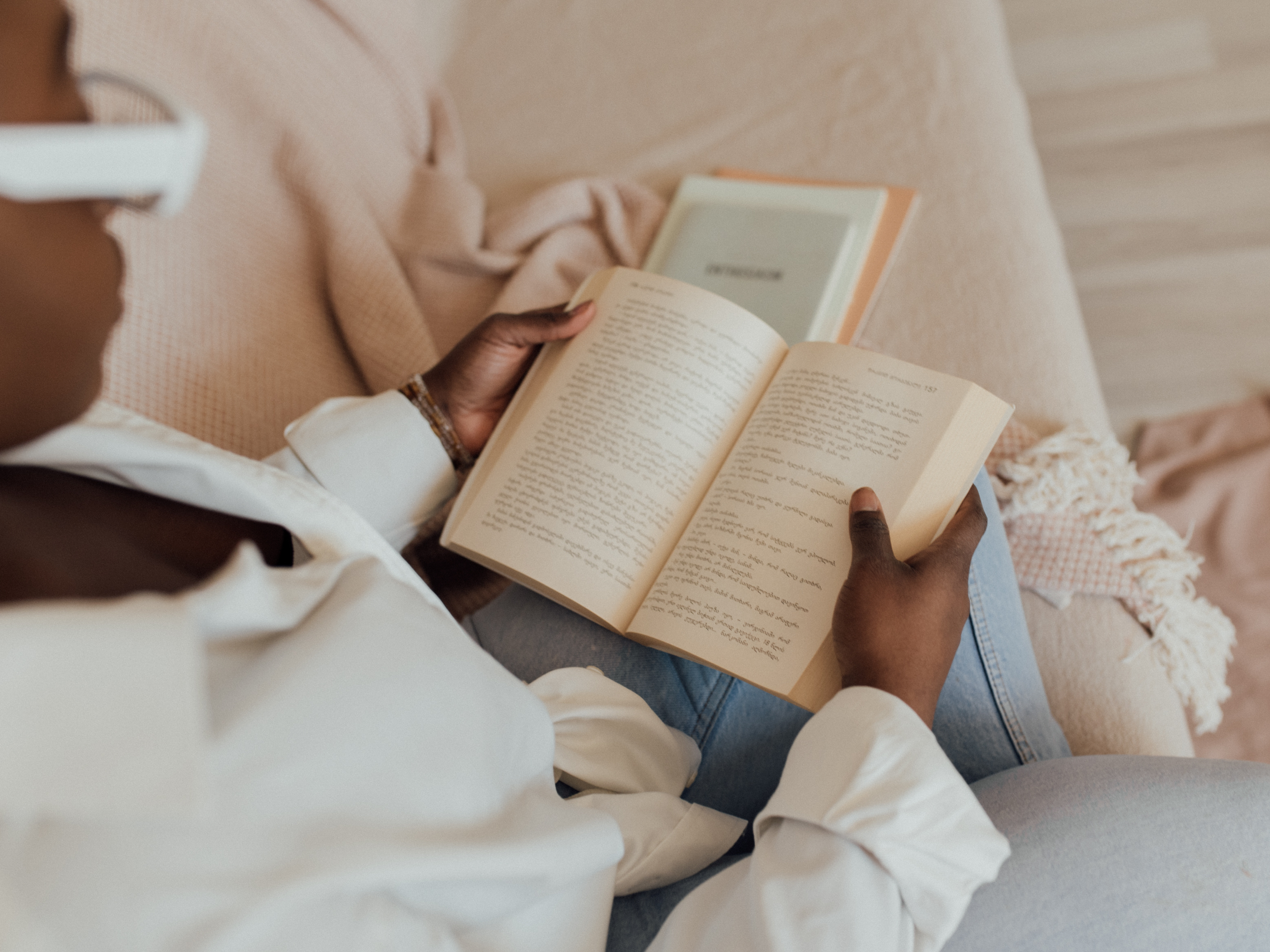 black woman with glasses sitting on couch reading a book
