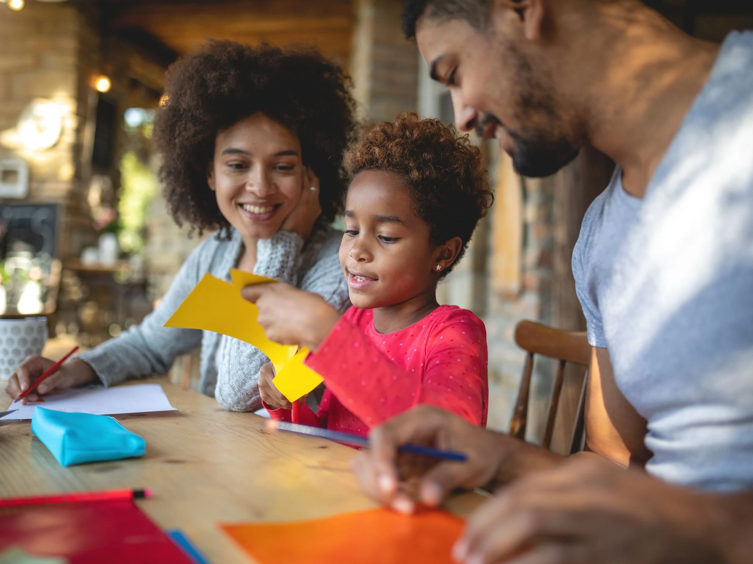 black mom, dad and daughter at table doing craft together