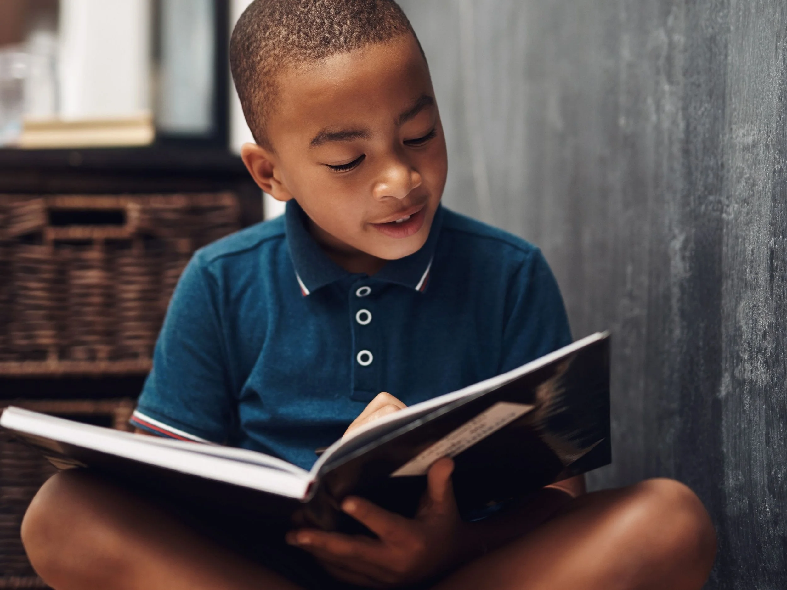 closeup of little black boy sitting on the floor and reading a book