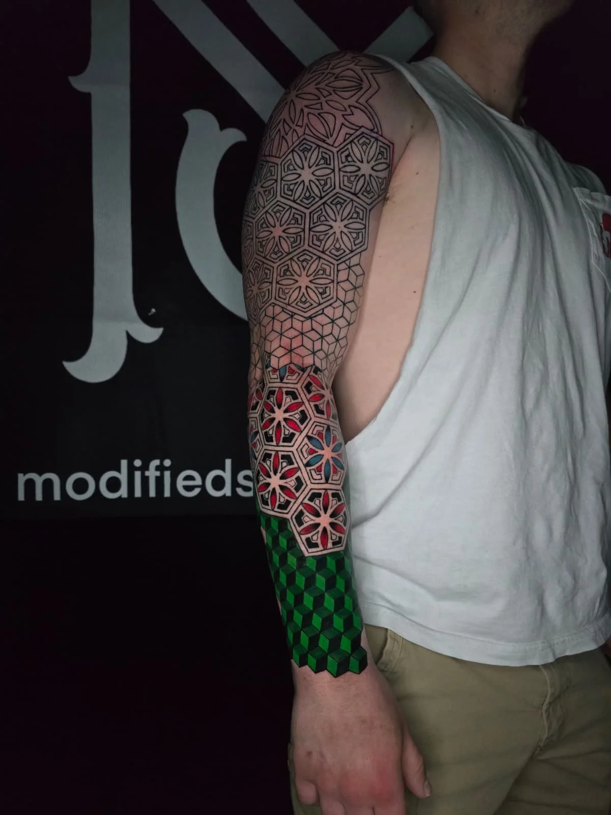 A person with a sleeve tattoo featuring geometric patterns in black lines, filled with colorful sections including red, blue, green, and black.