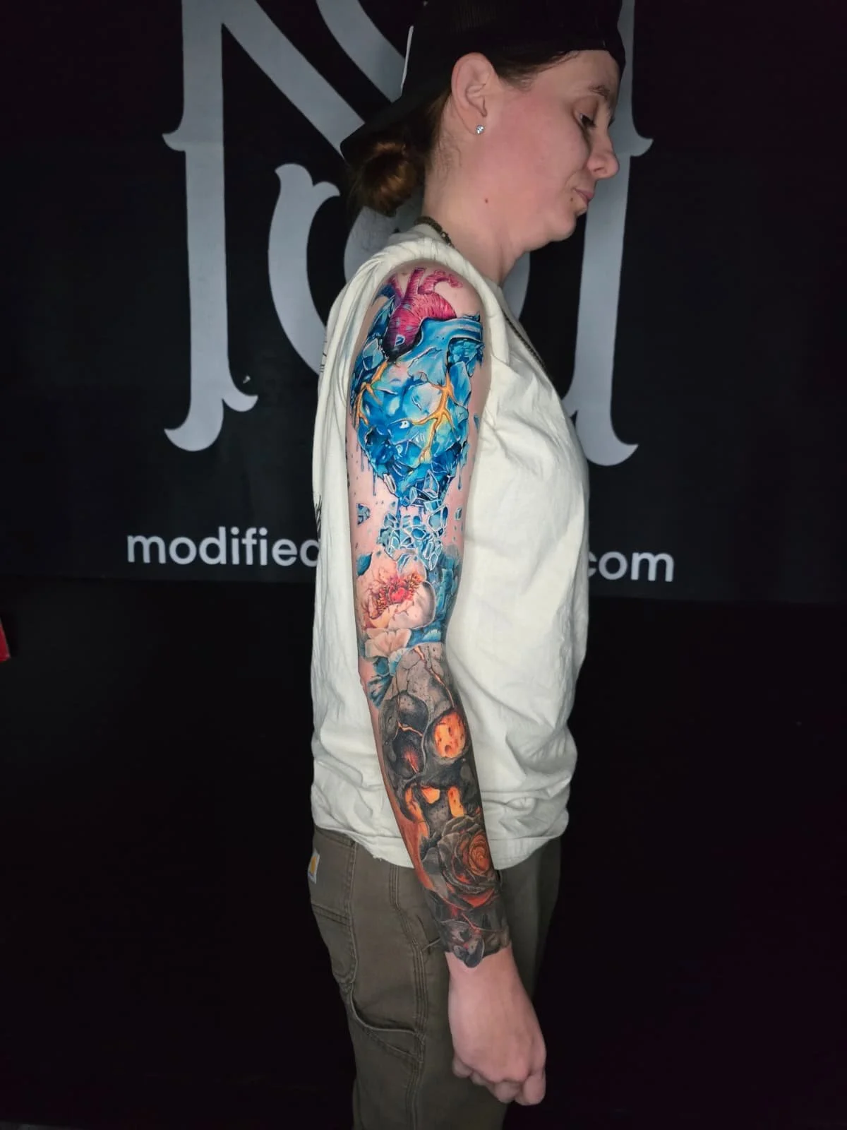 A woman with a colorful full sleeve tattoo standing in profile against a black background.