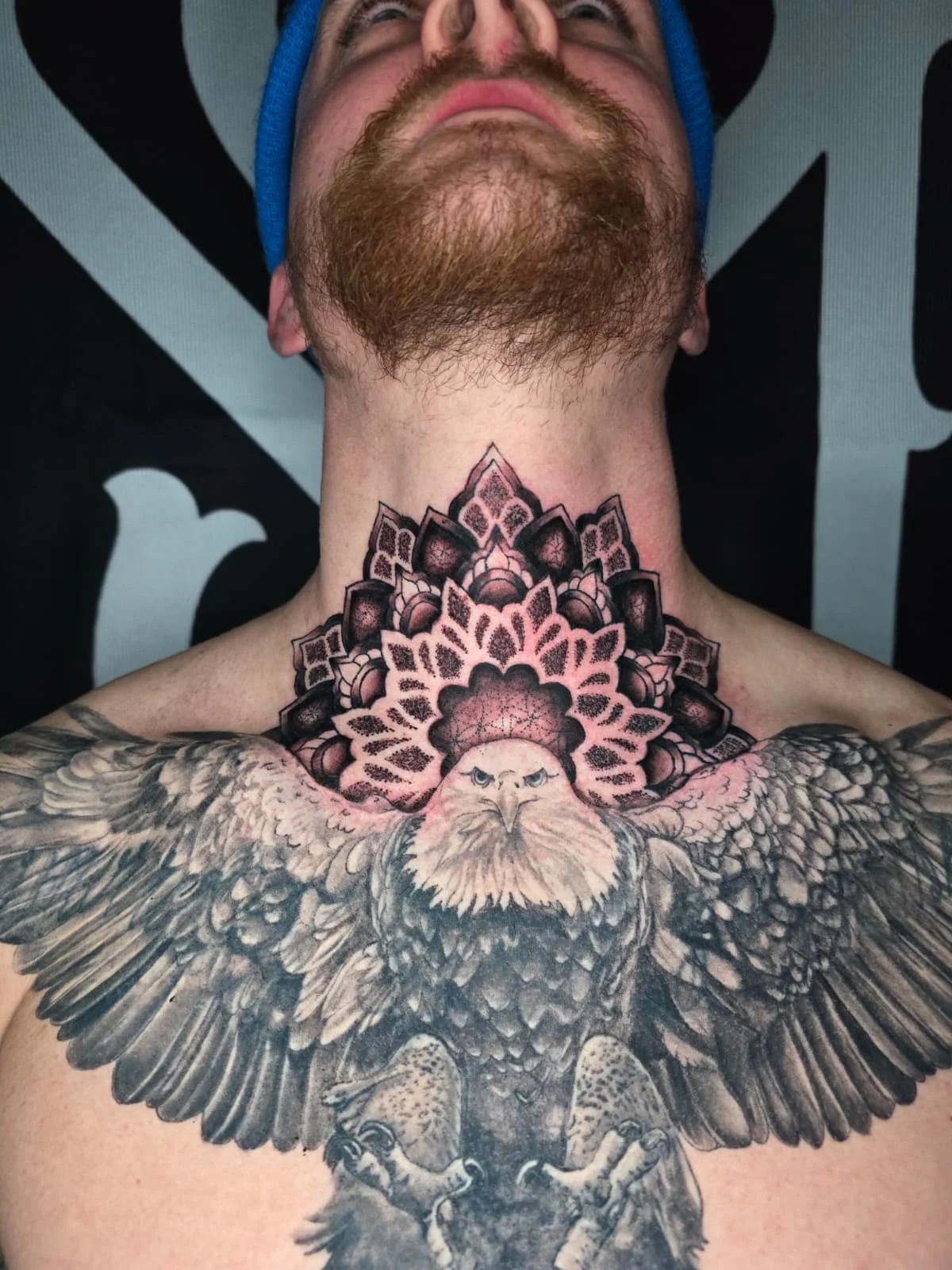 Close-up of a man's chest tattoo featuring a realistic bald eagle with its wings spread wide, and a stylized mandala design in the background.