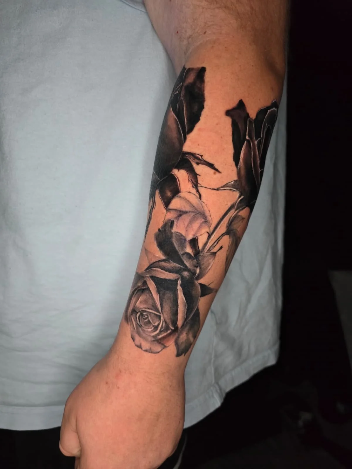 Black and gray realistic tattoo of a rose and leaves on a person's forearm.