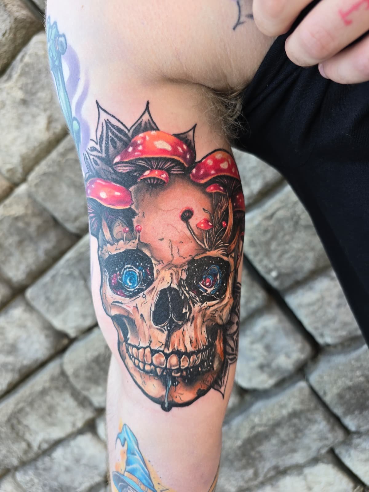 Tattoo of a skull with a background of red mushrooms and leaves, with cosmic galaxy eyes and a melting drip at the chin.