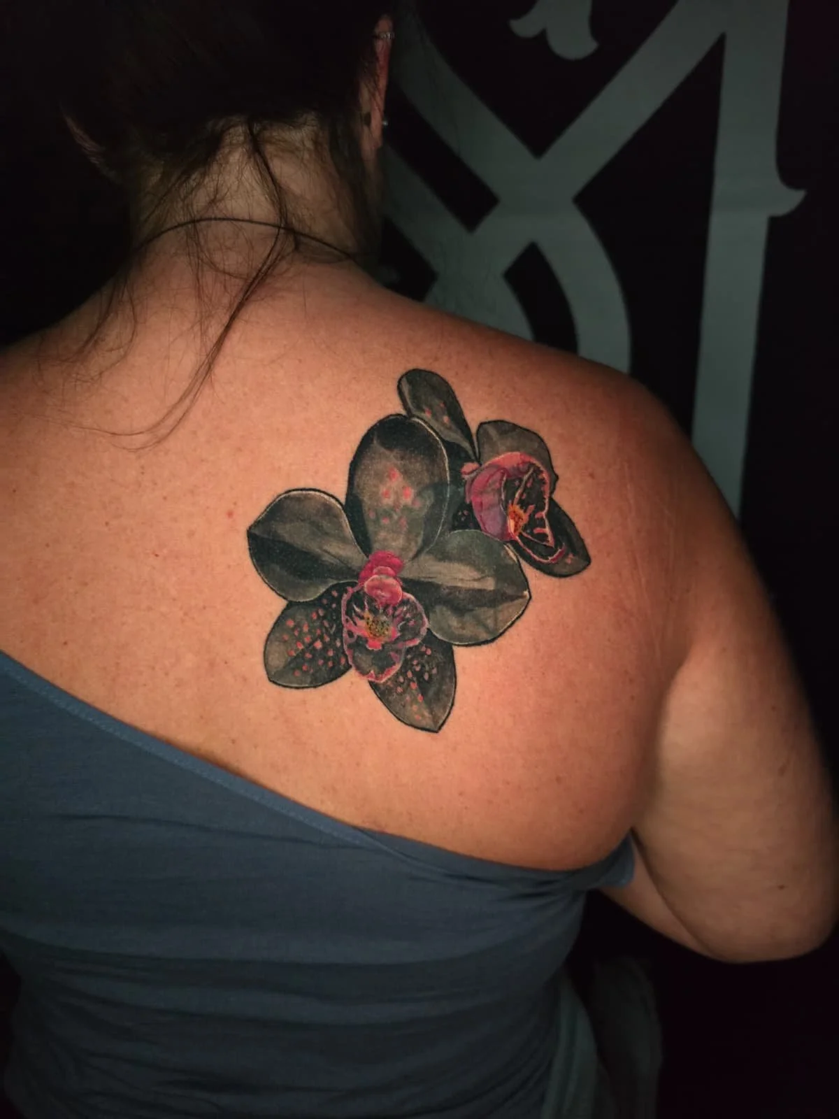 A tattoo of a black orchid flower with pink and red accents on a person's shoulder.