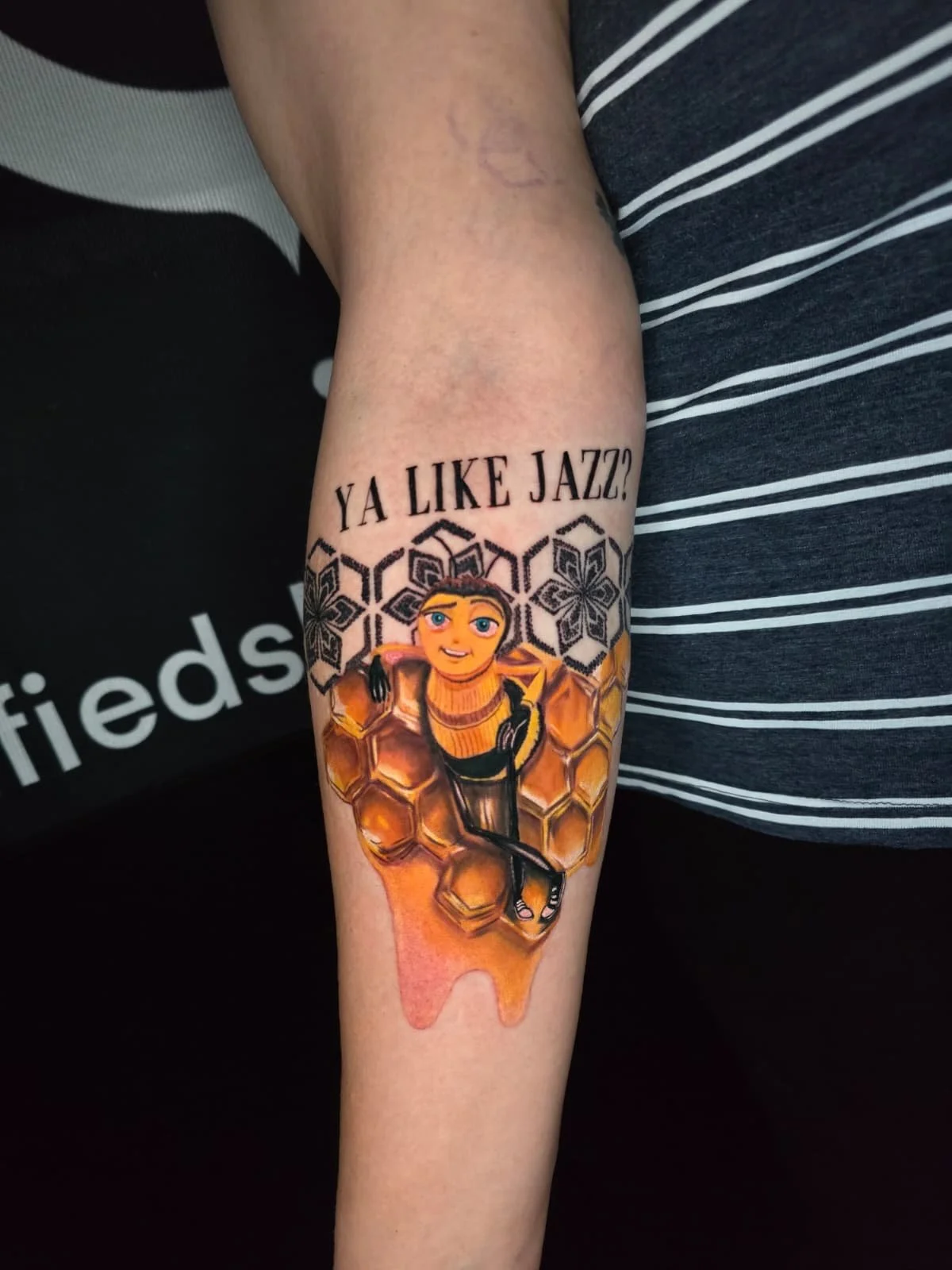Tattoo of a cartoon girl with orange hair and blue eyes sitting on a honeycomb with honey dripping below. Above the tattoo, text reads 'YA LIKE JAZZ?'