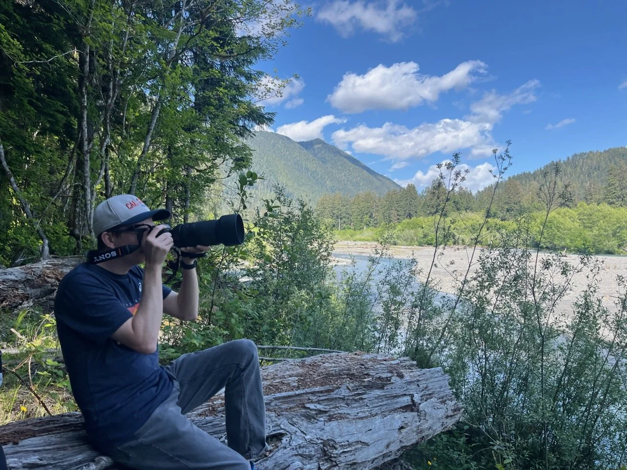 Tyler sitting on a large trunk with a telefoto lens taking photos of nature.