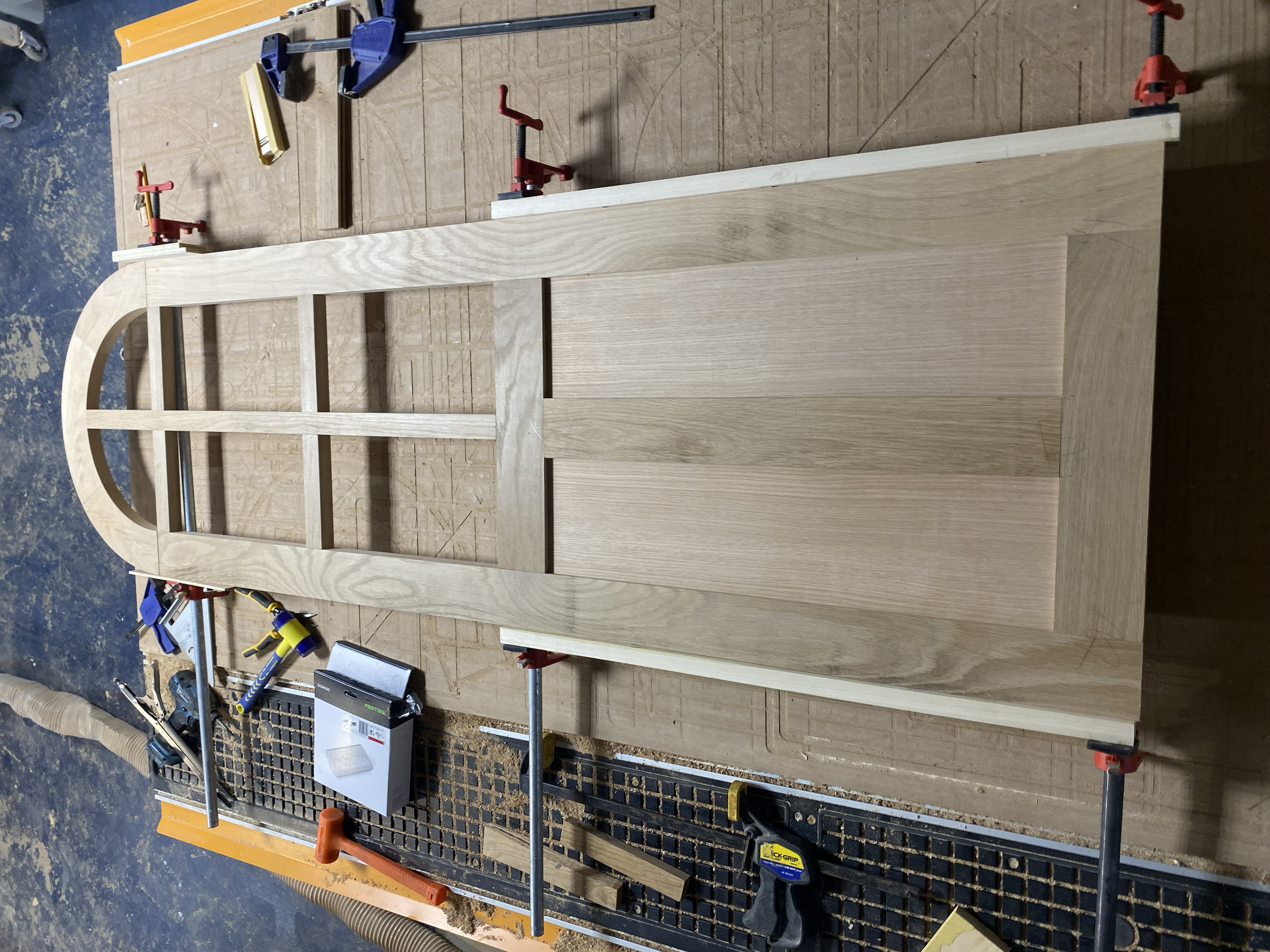 Wooden picture frame being assembled on a workbench with clamps, measuring tools, and woodworking supplies. DOOR. Custom Millwork.