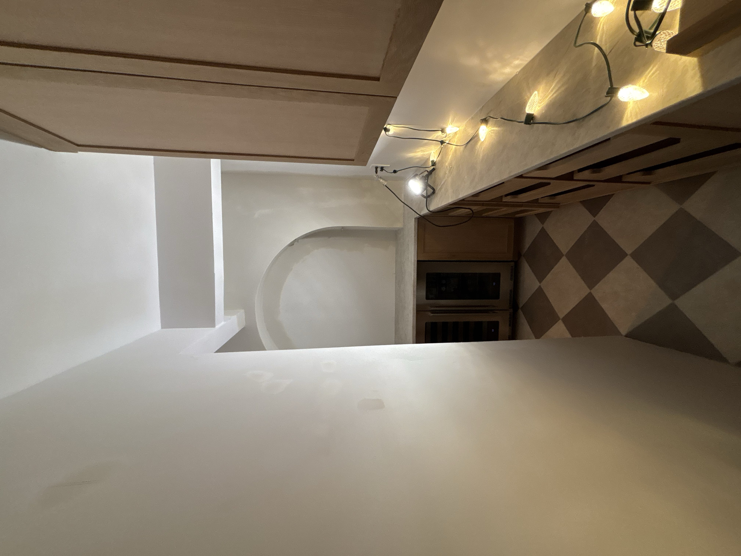 Interior view of a kitchen with a beige countertop decorated with string lights, wooden cabinets, and a patterned tile floor Walk in pantry. Custom Cabinetry.