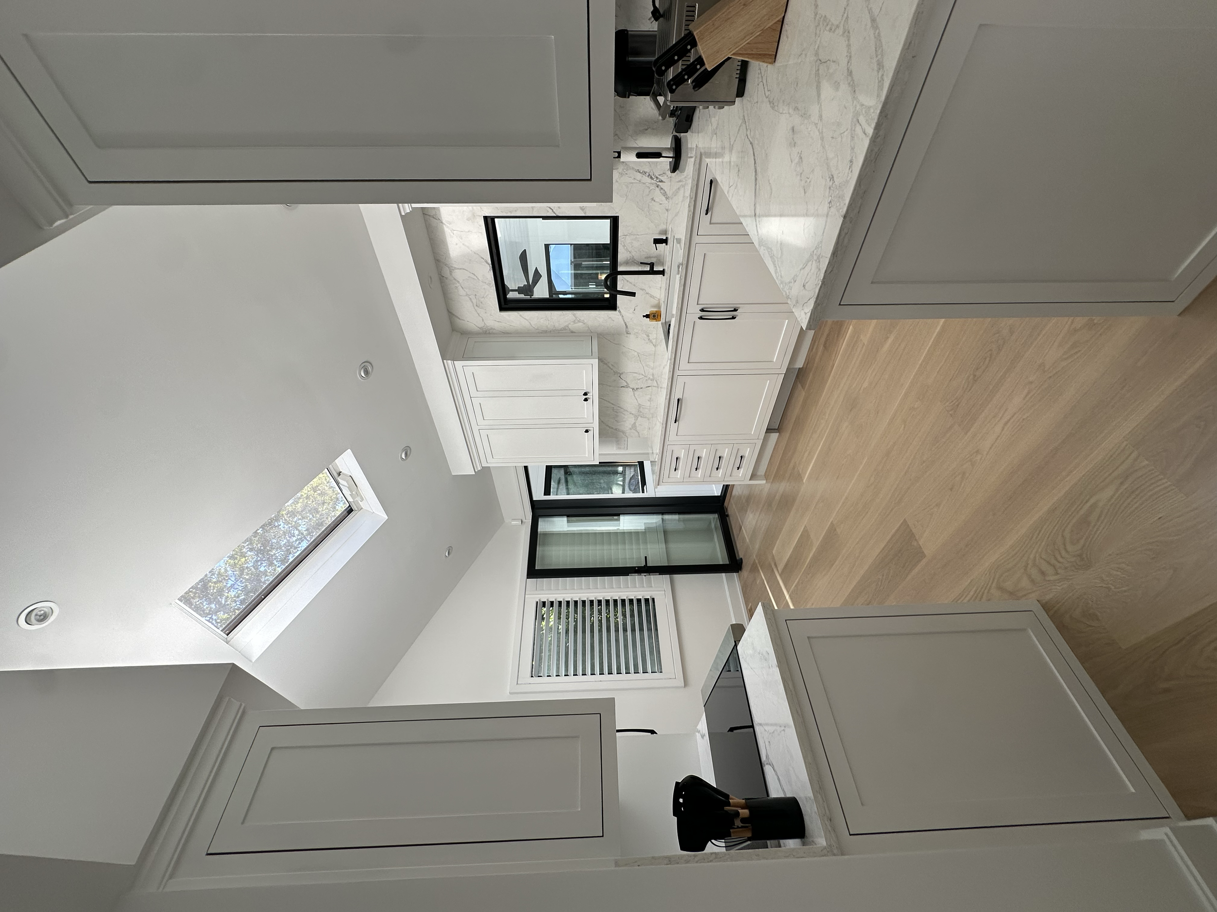 Modern kitchen with white cabinets, marble countertops, a double sink, and a large window and skylight bringing in natural light.