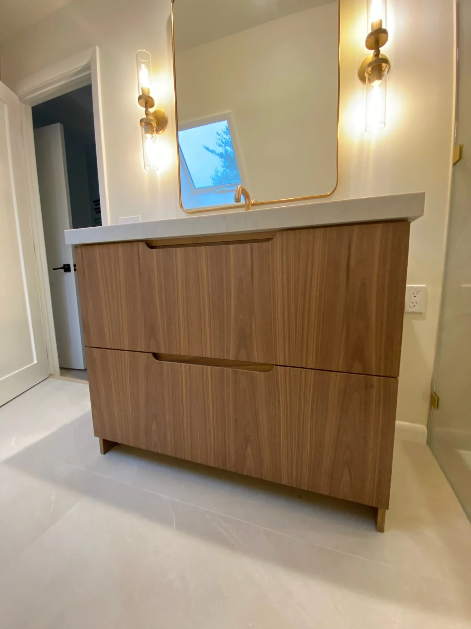 A modern bathroom vanity with a wooden cabinet, white countertop, mirror, and two wall sconces.