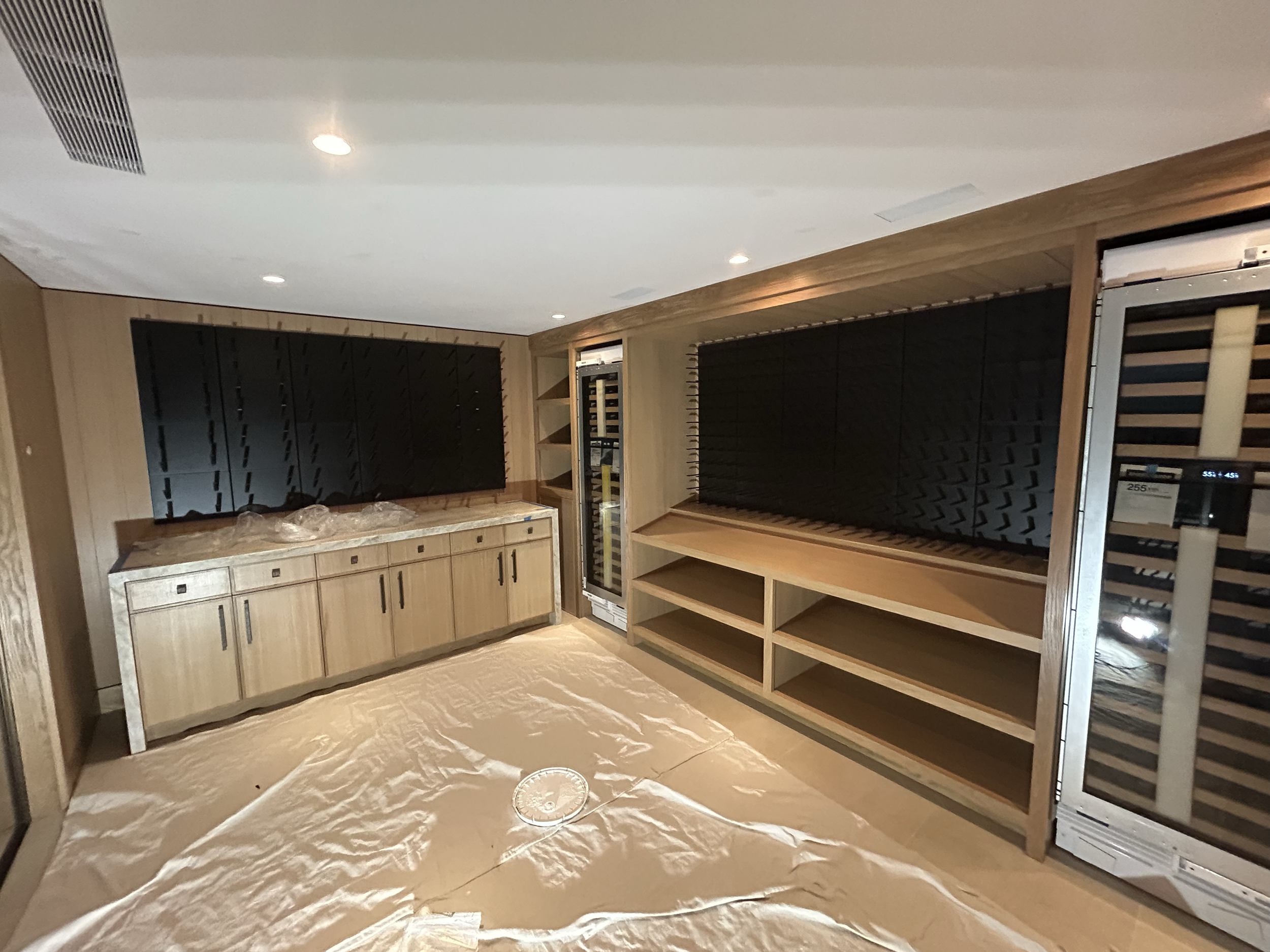 Interior view of a room with wooden cabinetry, shelves, and wine coolers, with black acoustic panels on the walls.