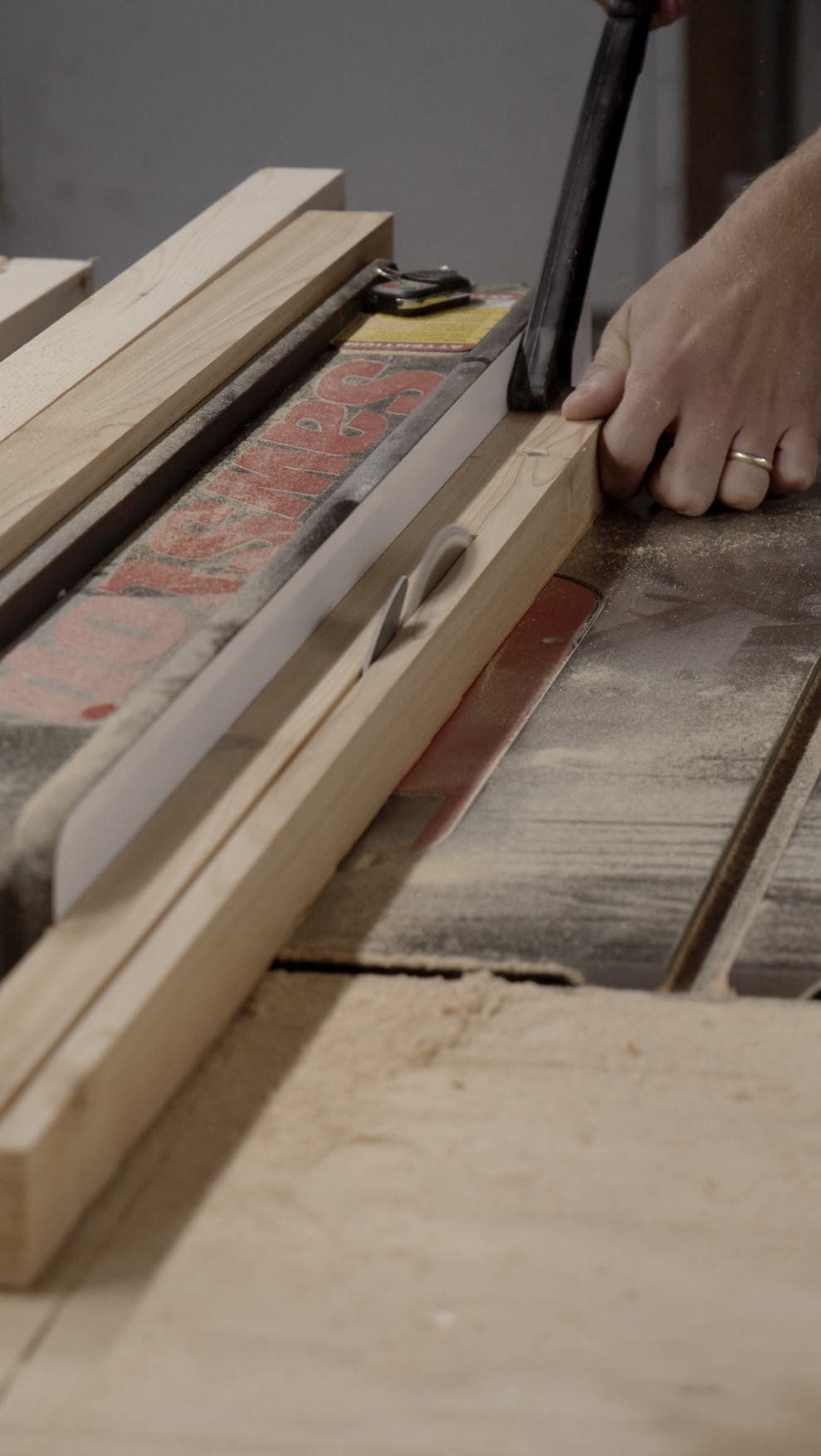 A person cutting a piece of wood with a saw on a workbench in a woodworking shop.
