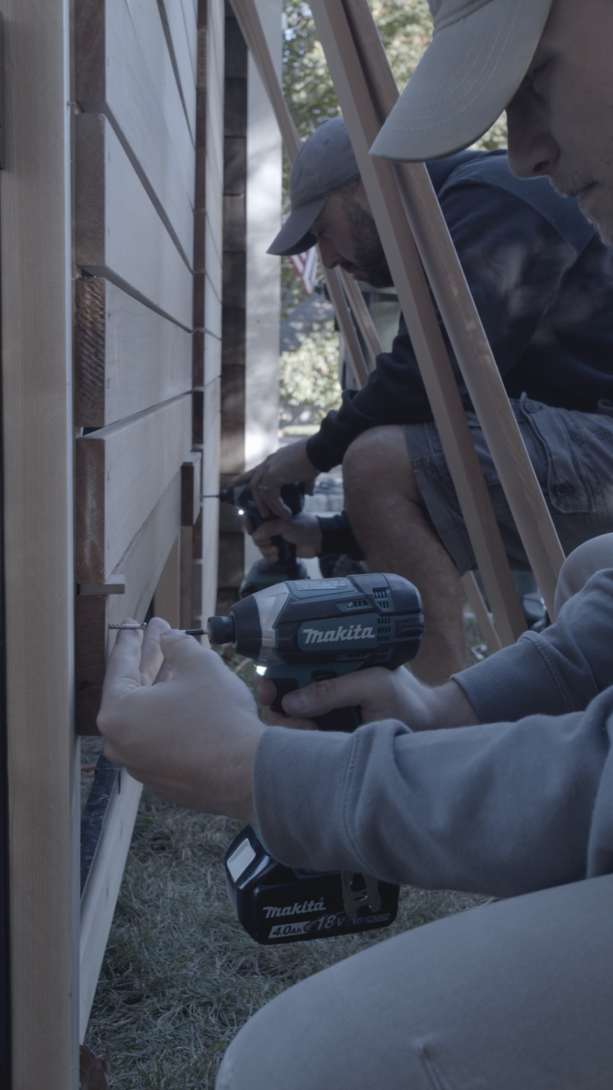 Two men working on a wooden structure outdoors using power drills. Fence project