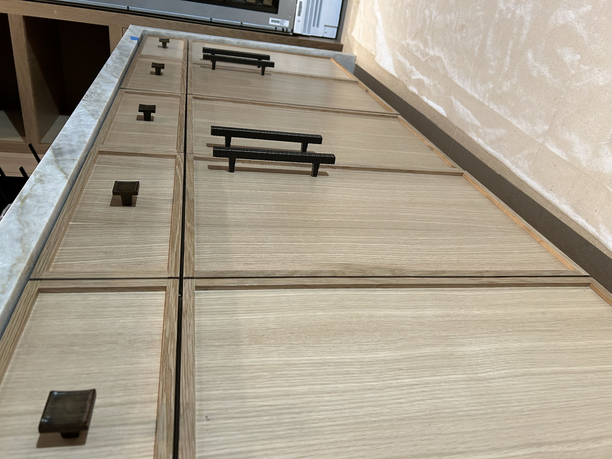 Wooden cabinets with black handles and a granite countertop section, with a beige tiled wall in the background.